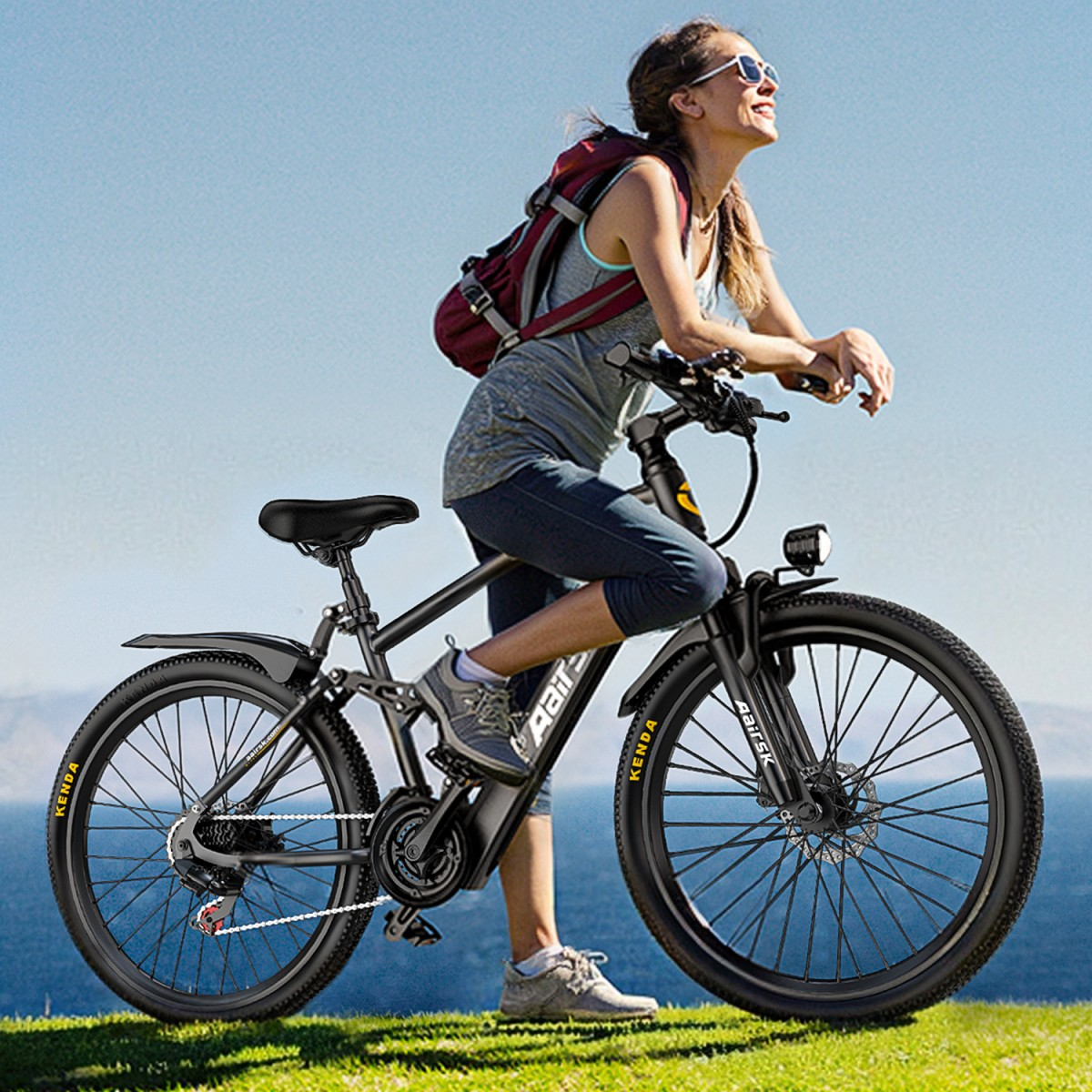 Eine Frau lehnt sich auf einer schwarzen Elektrofahrrad auf Gras. Sie trägt eine Sonnenbrille, einen Rucksack und lächelt in den blauen Himmel.