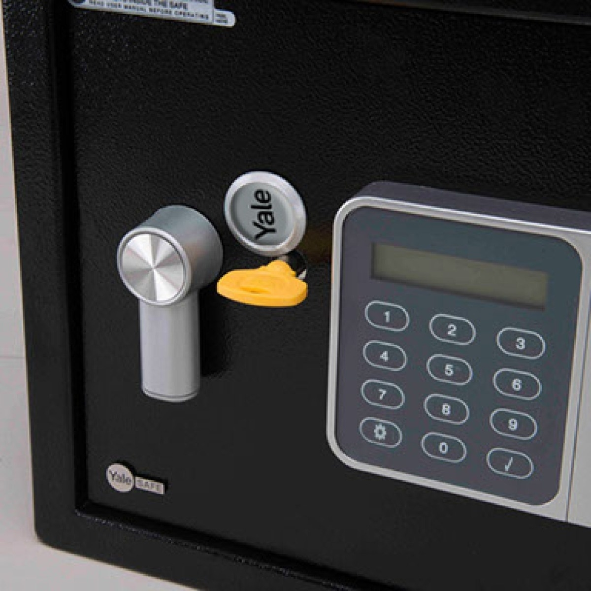 Cassaforte nera con tastierino digitale, serratura Yale e chiave. La chiave è gialla. La porta della cassaforte è chiusa.