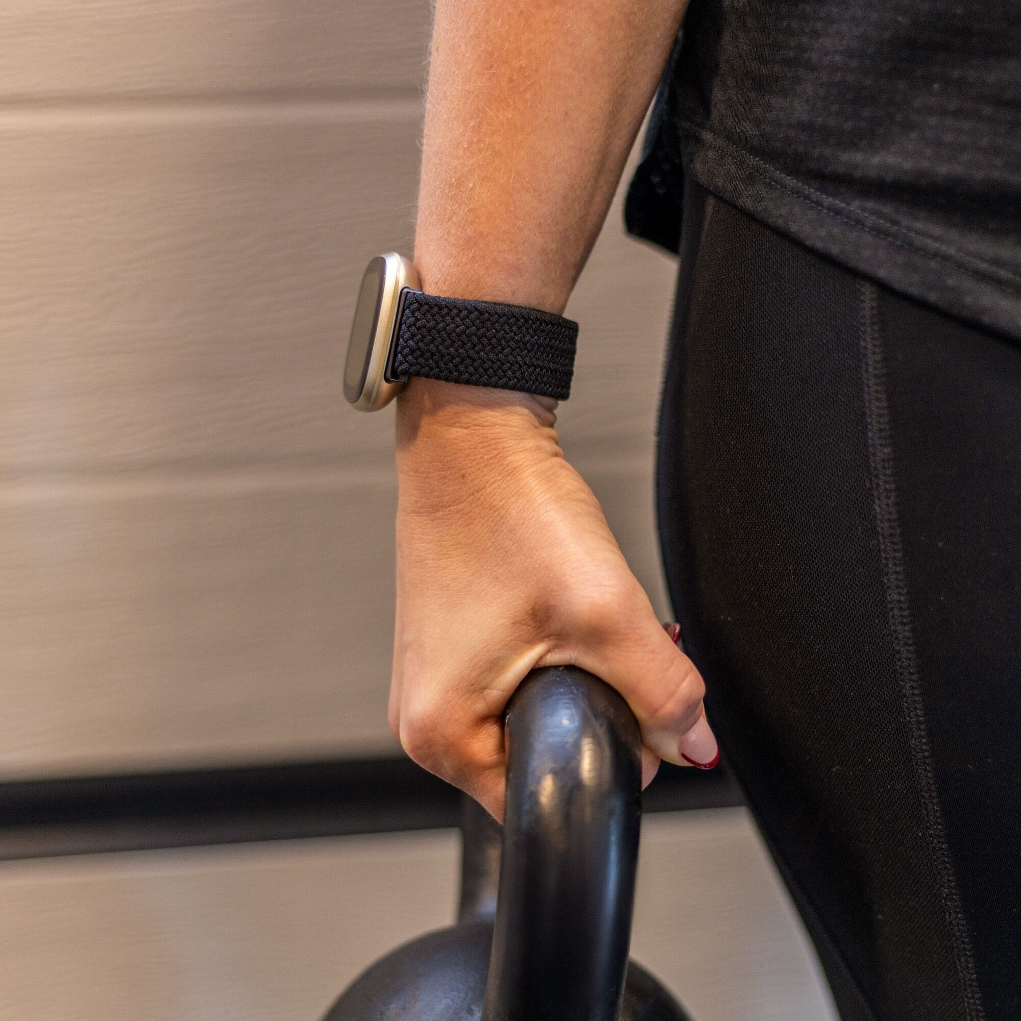 Person hält eine schwarze Kettlebell. Sie trägt eine Uhr, schwarze Trainingskleidung und hat roten Nagellack.