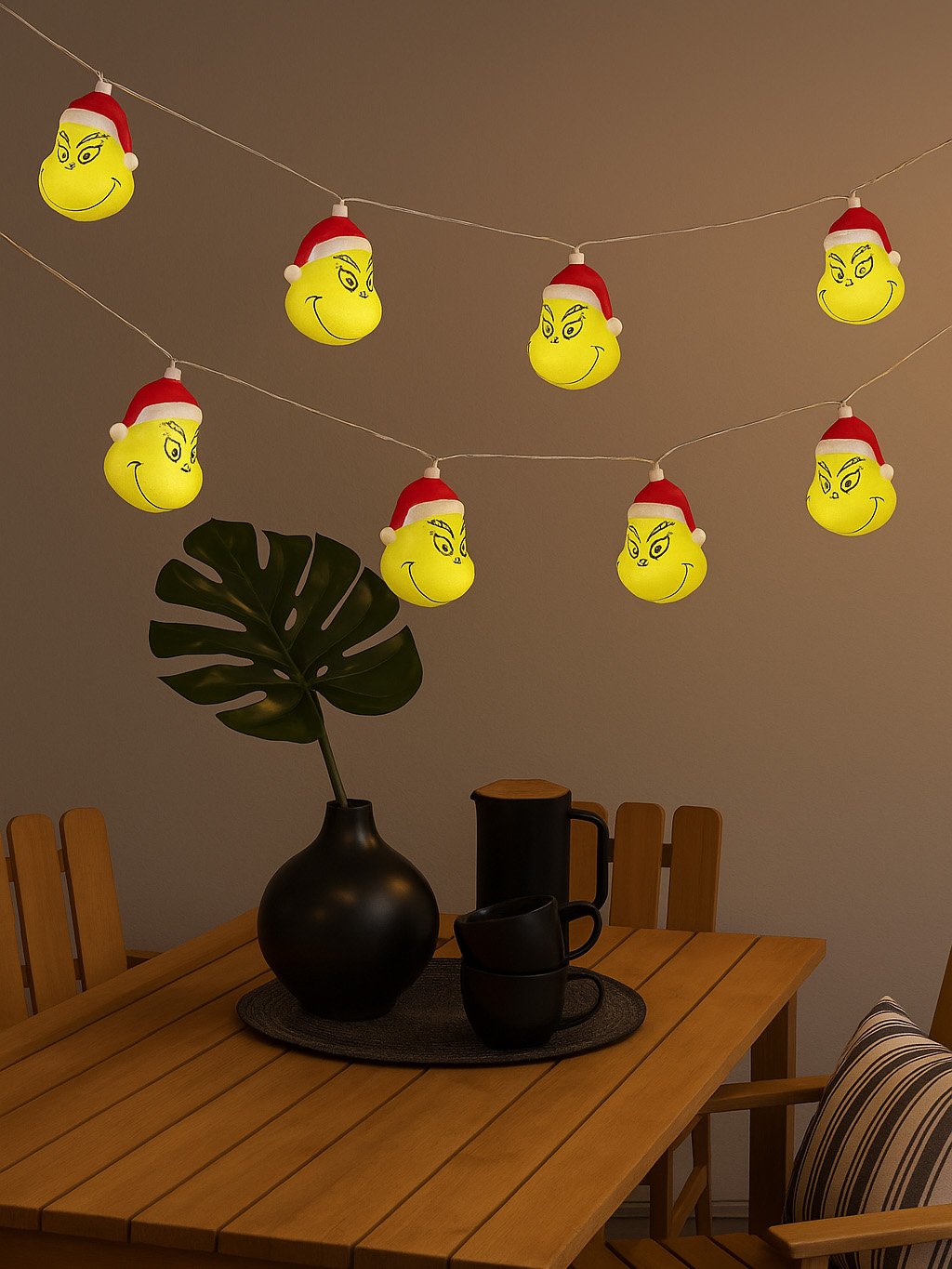 Grinch-Gesichter-Lichterkette über einem Tisch mit Dekoration. Eine Vase mit einer Pflanze, ein Tablett und Tassen stehen auf dem Tisch.