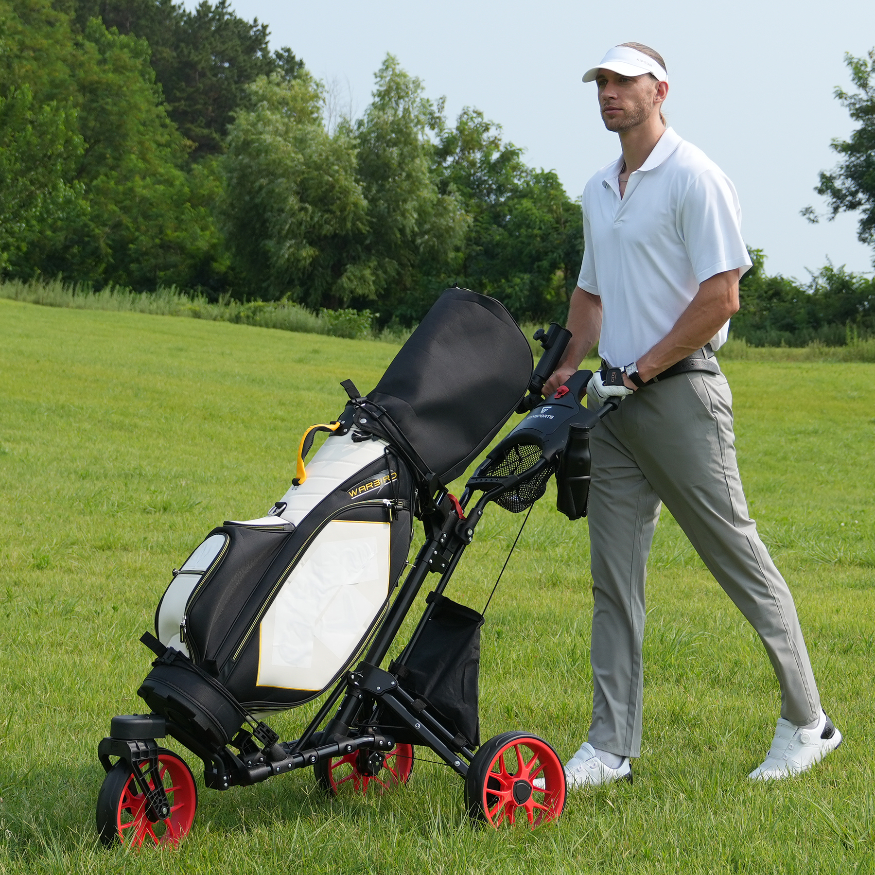 Mężczyzna w stroju do golfa pcha wózek golfowy na zielonym polu, w tle drzewa.