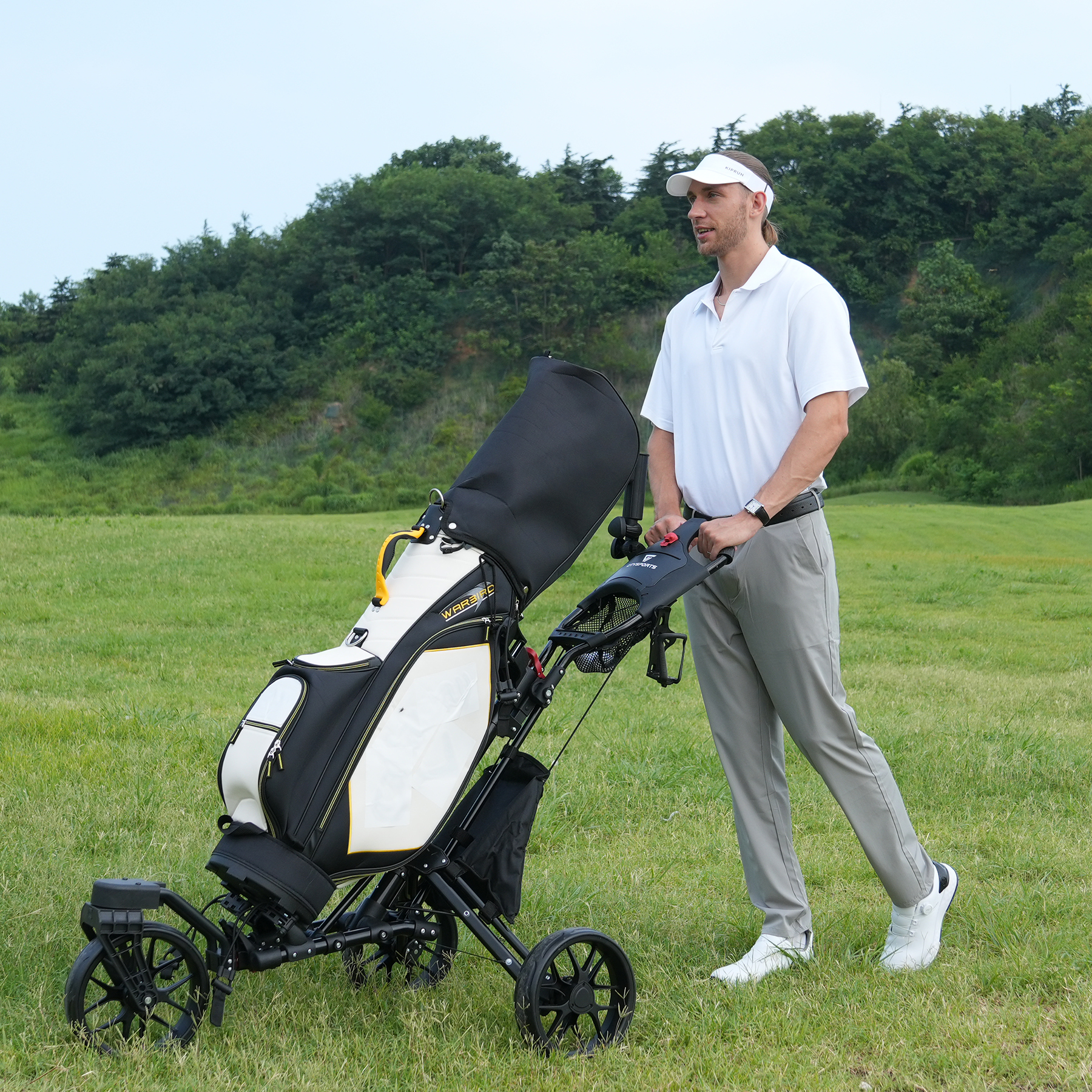 Mężczyzna w stroju golfowym pcha wózek golfowy z torbą golfową na zielonym polu. W tle drzewa.