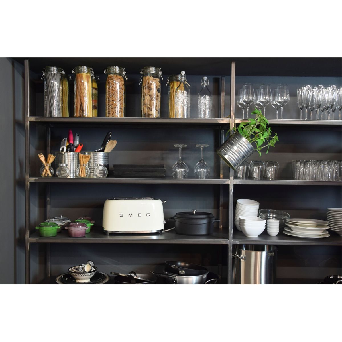 Półki kuchenne ze słoikami z jedzeniem, szkłem, tosterem, garnkami i przechyloną rośliną. Półki są ciemnoszare.