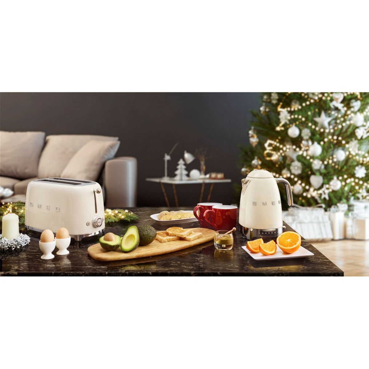 Scena śniadania z tosterem, czajnikiem, awokado, tostami, pomarańczami i choinką w tle. Czerwone kubki i jajka na stole.