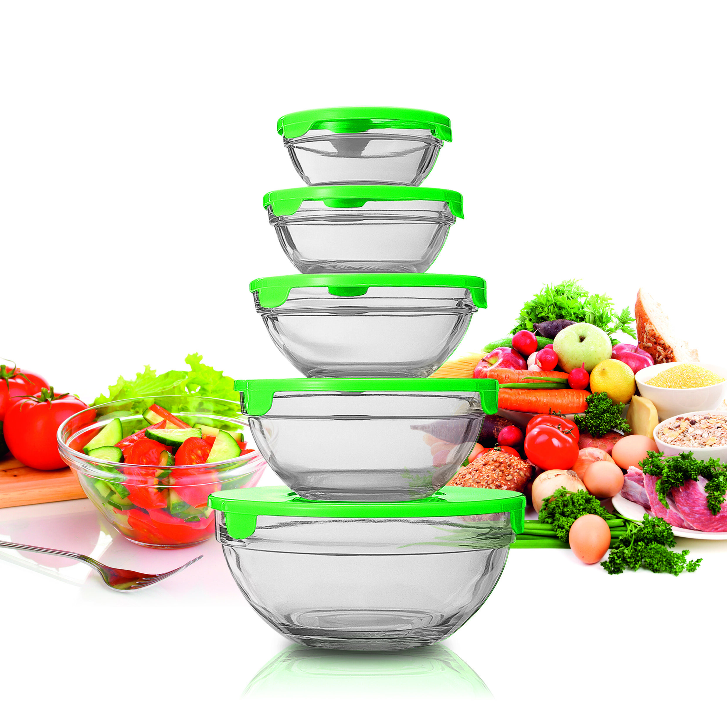 Cuencos de vidrio con tapas verdes apilados. Verduras y alimentos los rodean, incluida una ensalada.