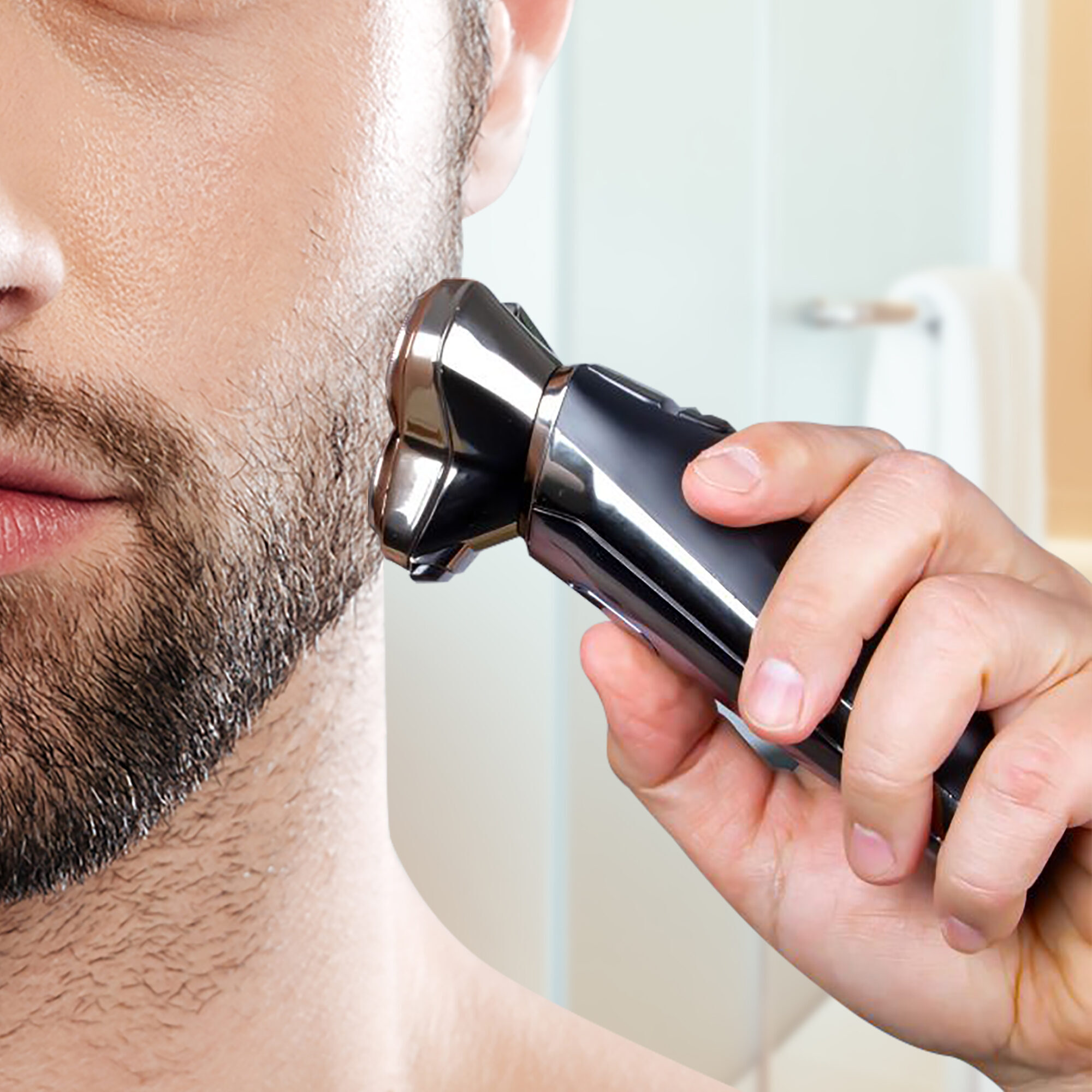 Un uomo si rade la barba con un rasoio elettrico. Il rasoio è nero e argento.