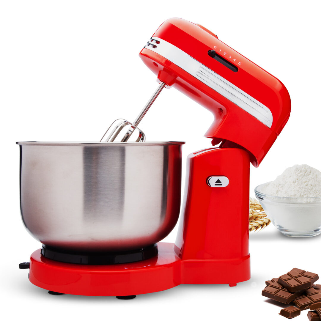 Un mixer rosso con ciotola in acciaio inox, farina, cioccolato e grano. Il mixer è su sfondo bianco.