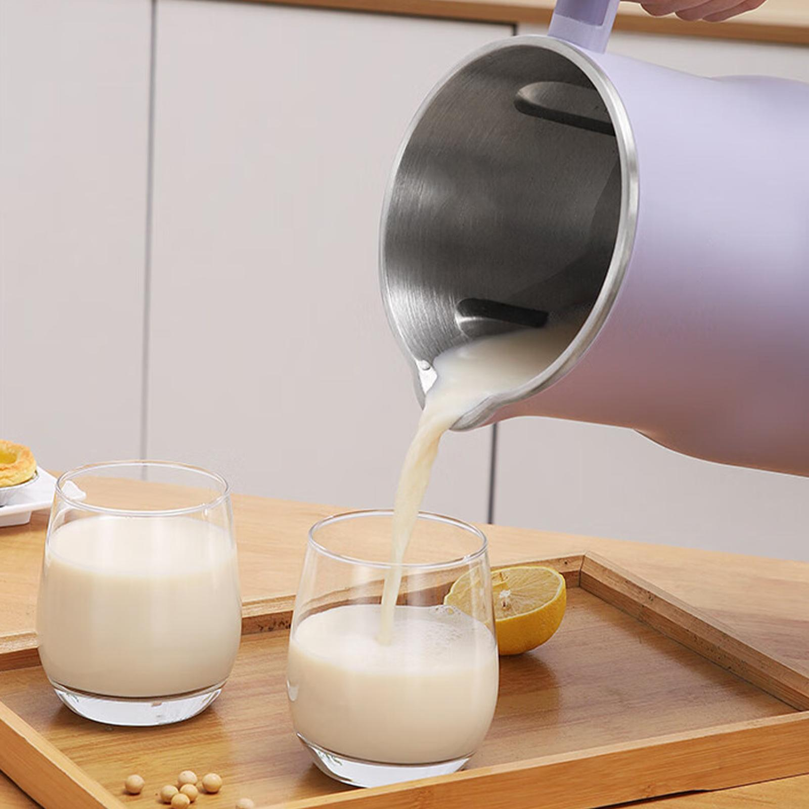 Ein lila Krug gießt Milch in ein Glas. Zwei Gläser mit Milch, eine Zitrone und Sojabohnen stehen auf einem Holztablett.