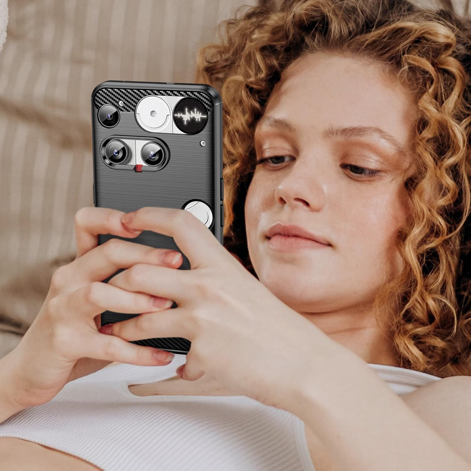 Eine Frau mit lockigem Haar hält ein Handy mit einer einzigartigen Hülle. Sie schaut nach unten. Das Telefon hat mehrere Kameralinsen.
