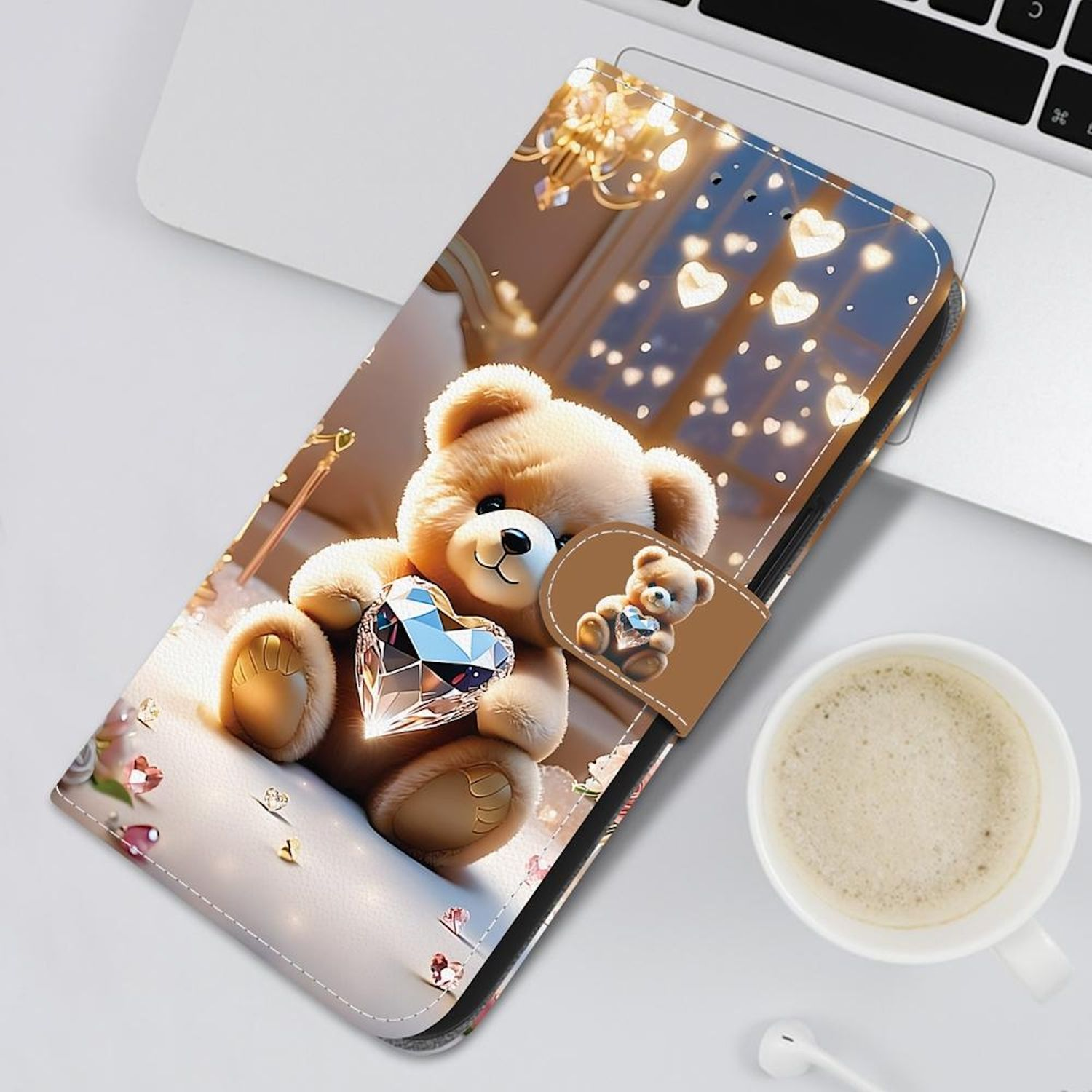 Ein Teddybär, der ein Diamantenherz hält, befindet sich auf einer Handyhülle, neben einer Kaffeetasse und einem Laptop.