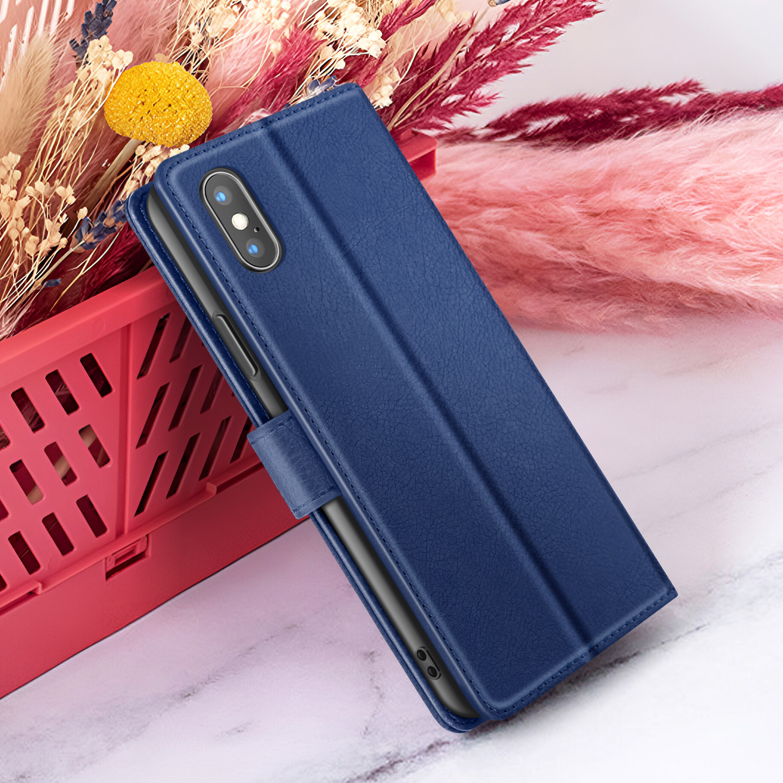 Een blauwe telefoonhoes met camera staat op een rode mand naast een roze en beige bloemstuk.