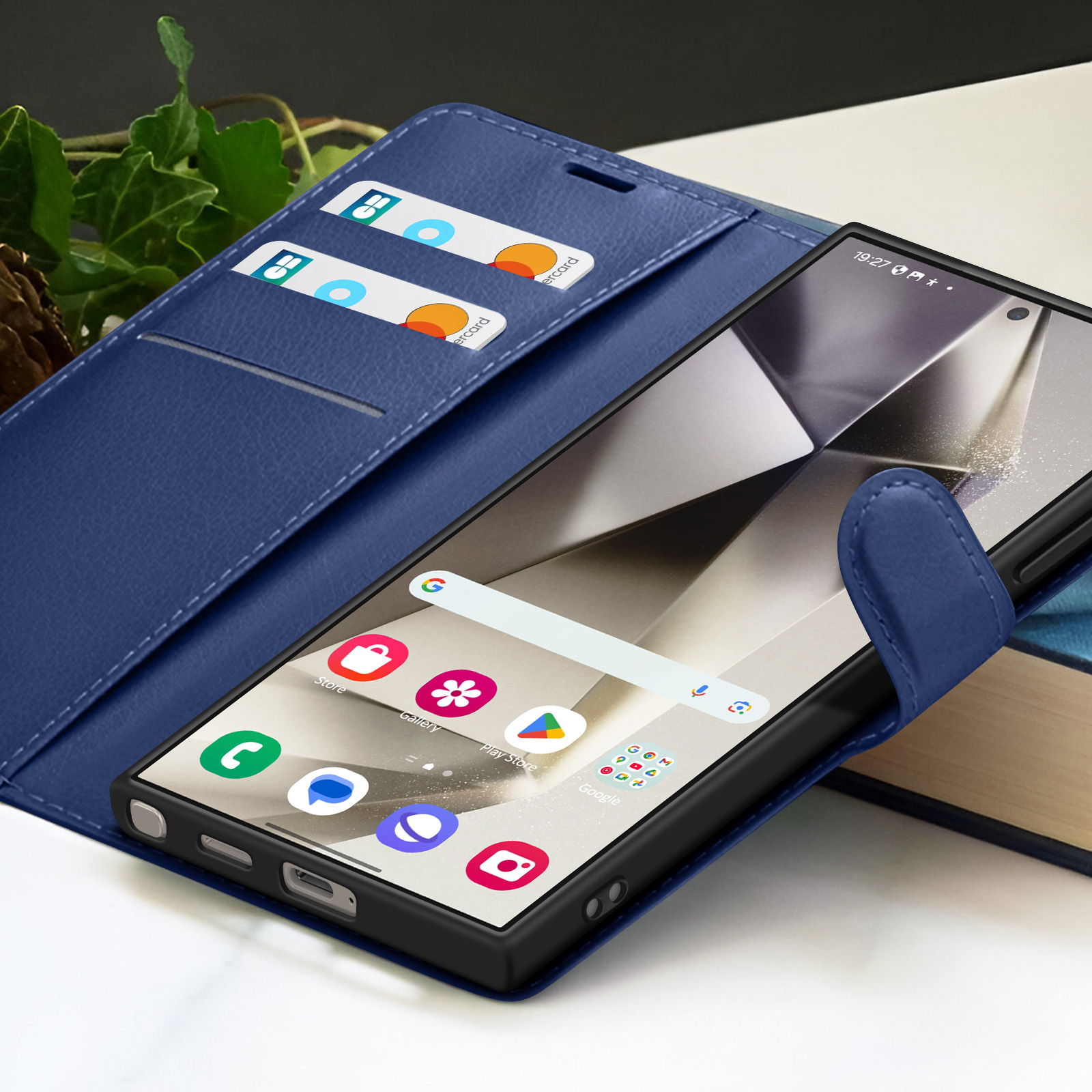 Smartphone in een blauwe leren hoes met kaarten. Het scherm toont app-iconen. Achtergrond: boek en groene bladeren.