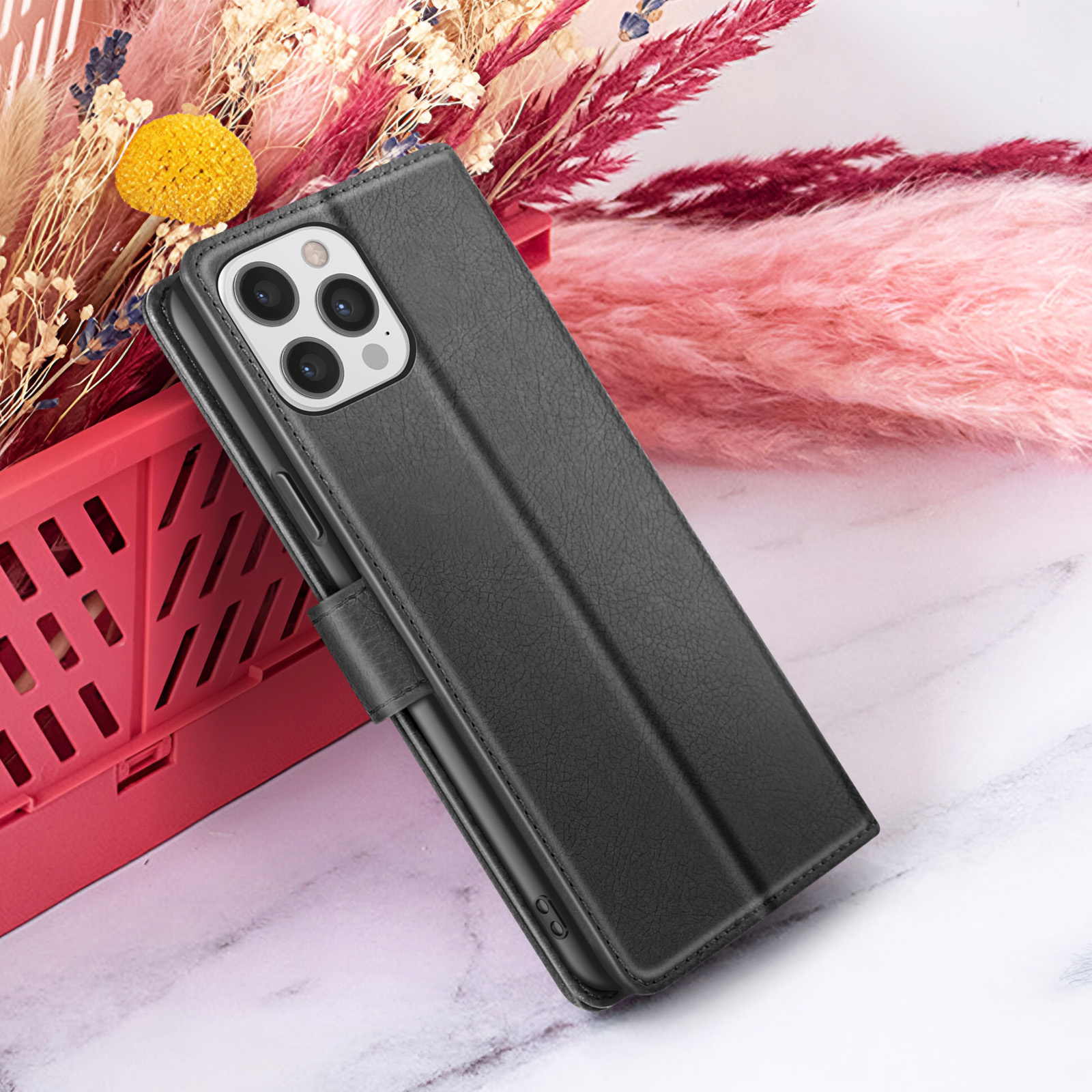 È mostrata una custodia per telefono nera con patta, con un bouquet di fiori rosa e beige sullo sfondo su una superficie di marmo.
