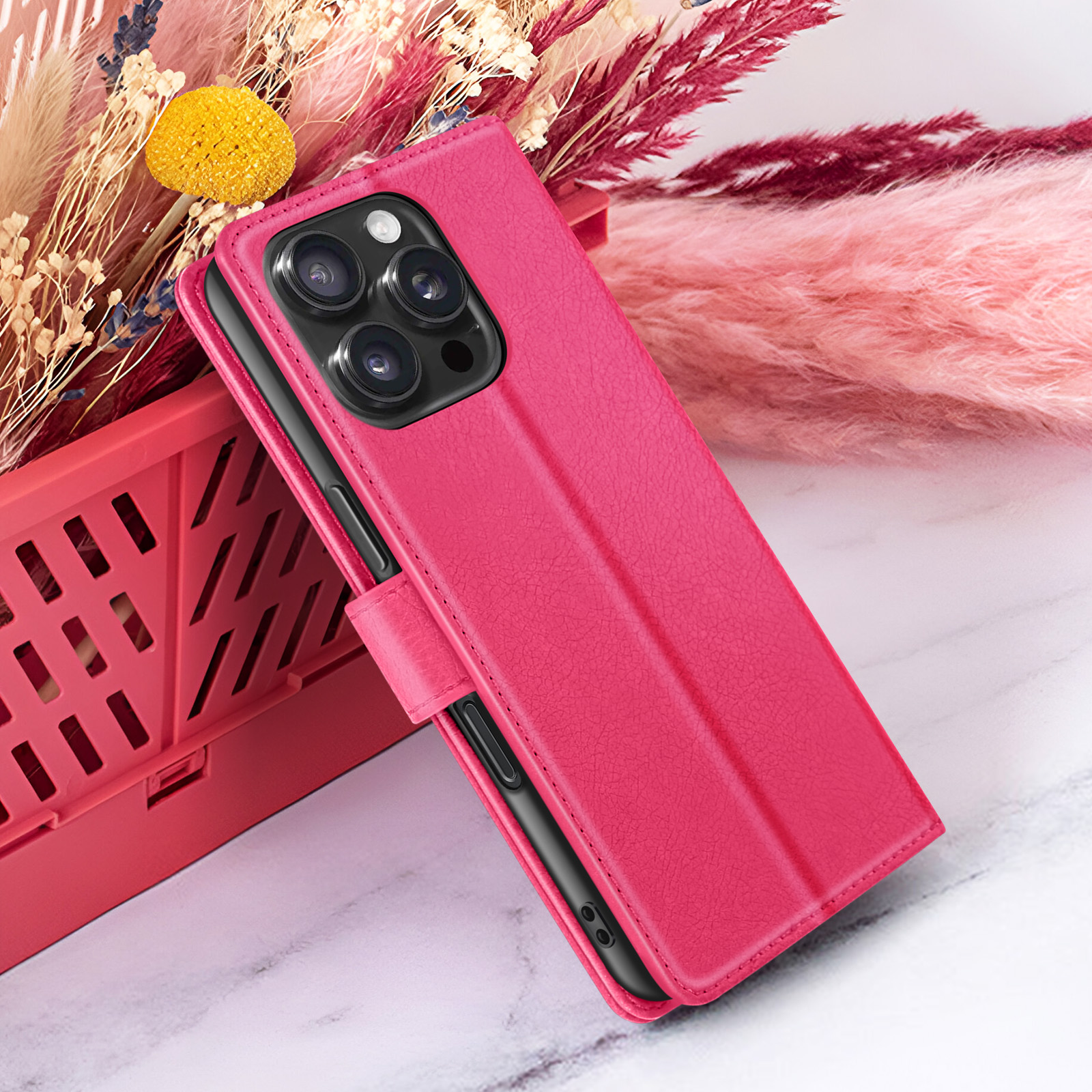 Een roze telefoonhoesje met een zwarte telefoon erin, op een marmeren oppervlak, met een roze en beige bloemenachtergrond.