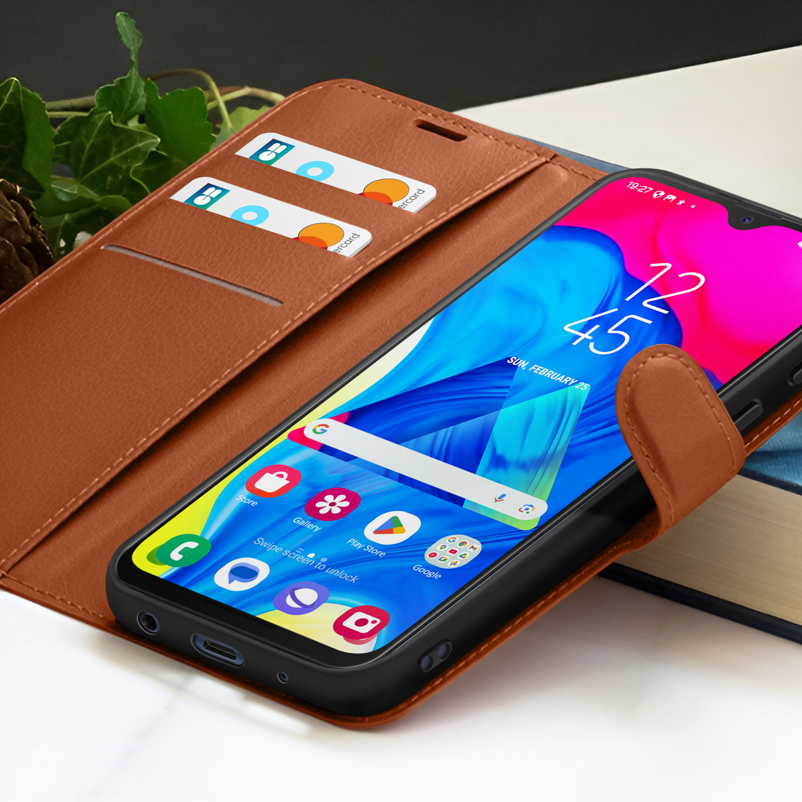Un smartphone dans un étui en cuir marron affichant l'heure. Deux cartes de crédit sont dans l'étui. Un livre est en arrière-plan.