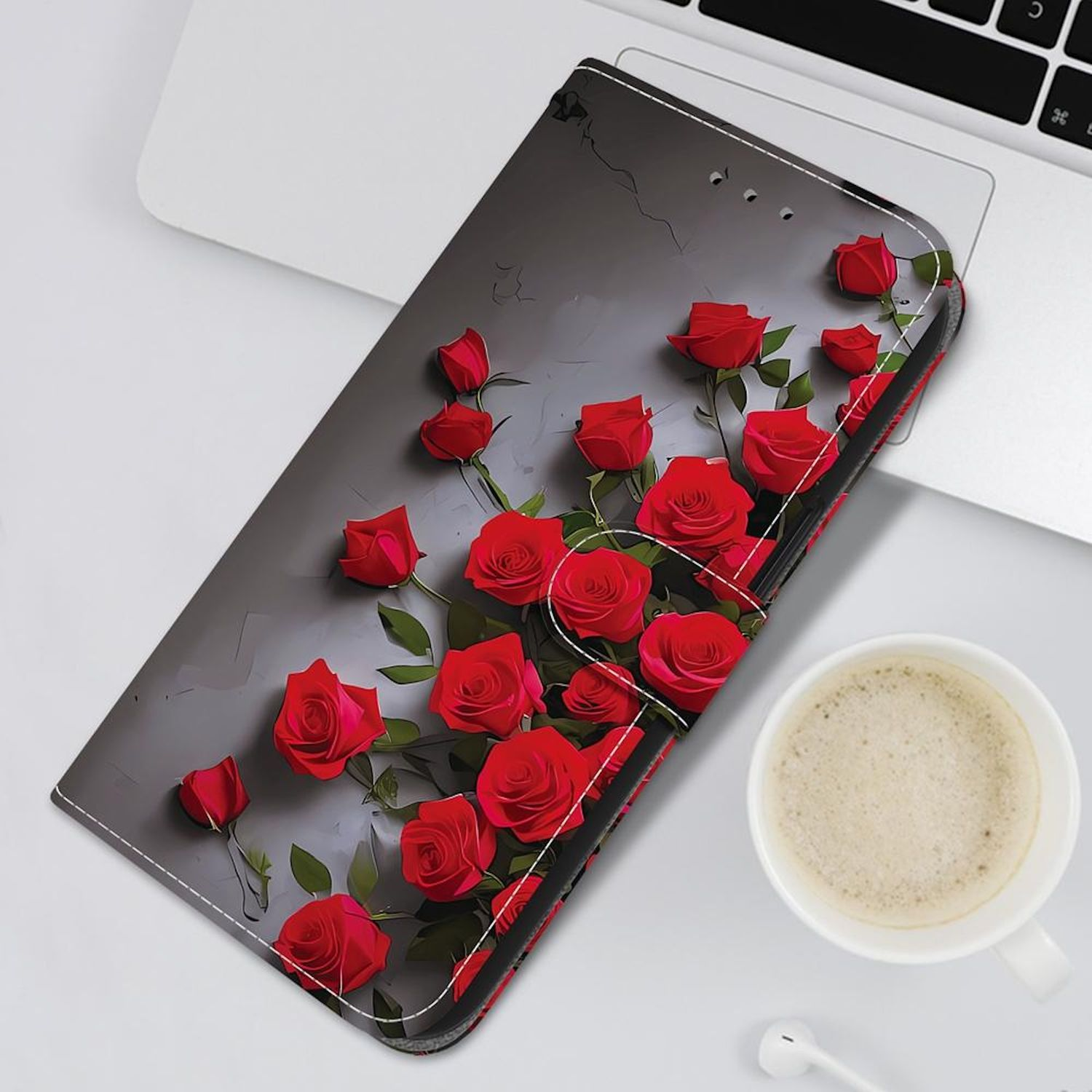 Eine Handyhülle mit roten Rosen liegt auf einem Laptop. Eine Tasse Kaffee und ein Ohrhörer sind daneben.