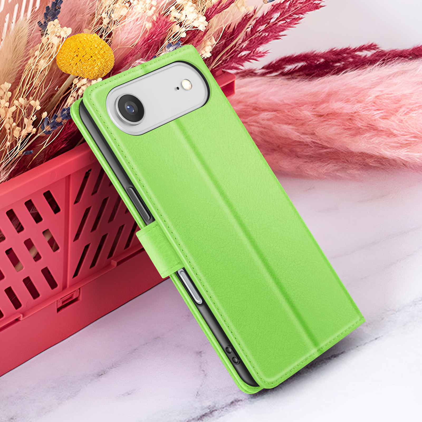 Una custodia verde per telefono con il telefono dentro, posizionata su un cestino rosso e fiori.