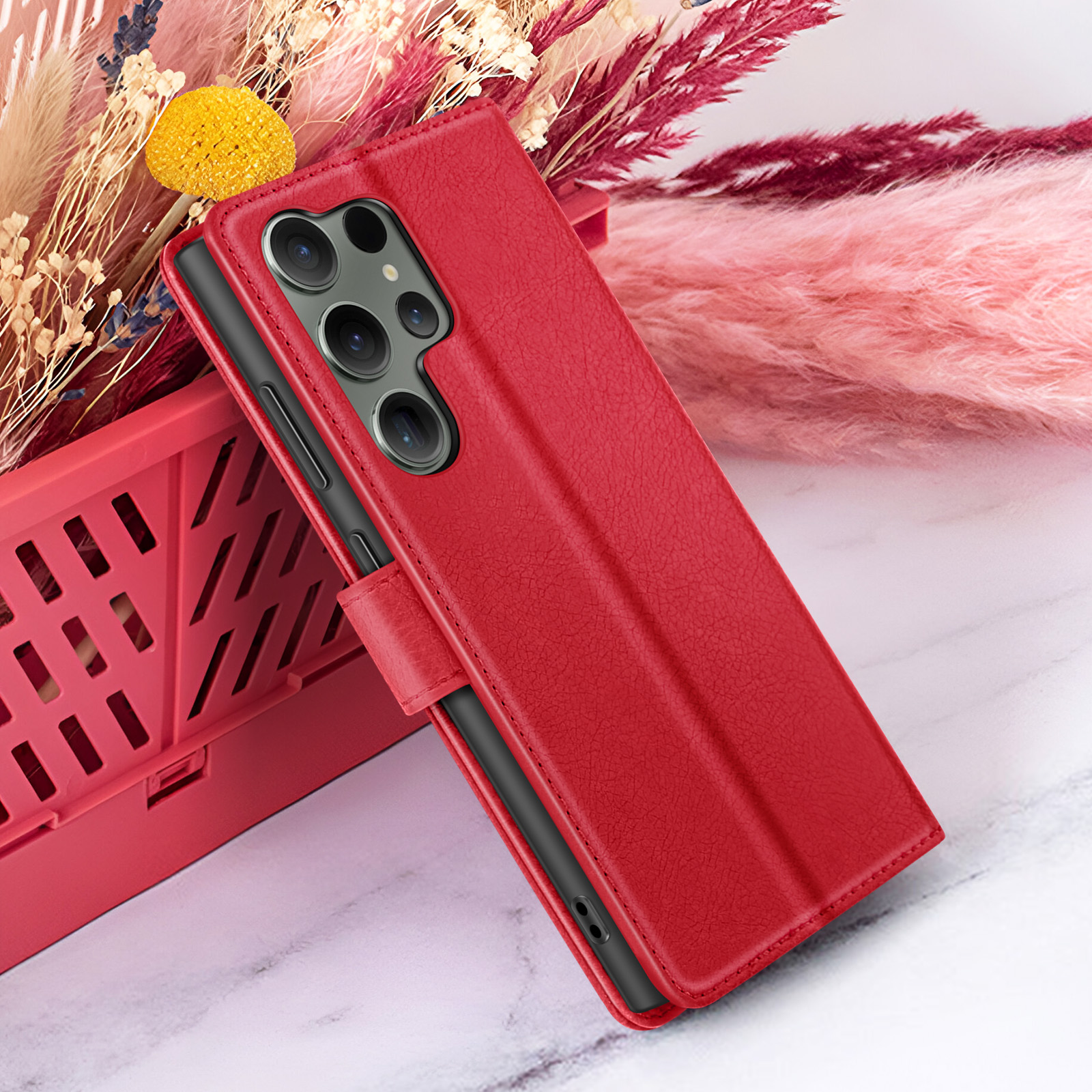 Een rode telefoonhoes met meerdere camera's is open, rustend op een marmeren oppervlak, omringd door gedroogde bloemen.