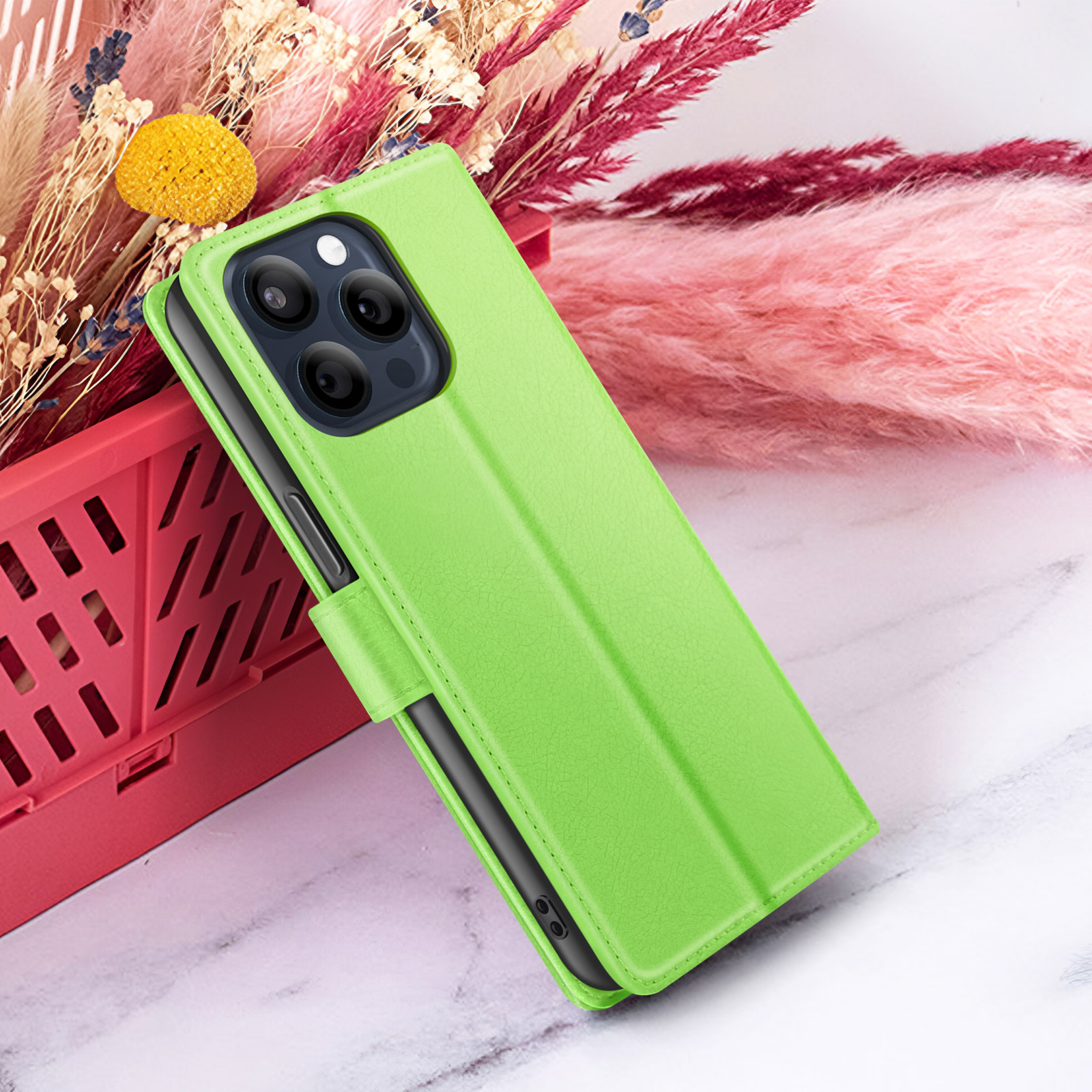 Een limoengroene telefoonhoes met een telefoon erin, geplaatst voor roze en kastanjebruine bloemen. De achtergrond is wit.