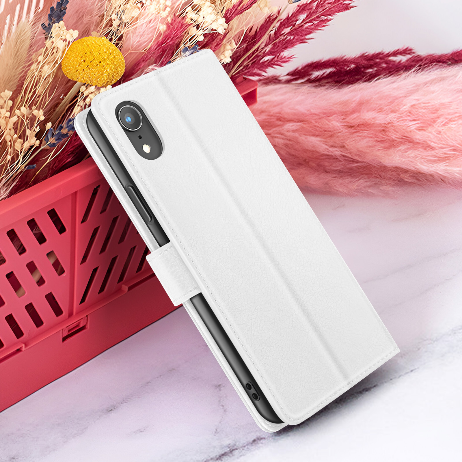 Weiße Handyhülle mit Telefon, roter Korb mit Blumen im Hintergrund, Marmoroberfläche.