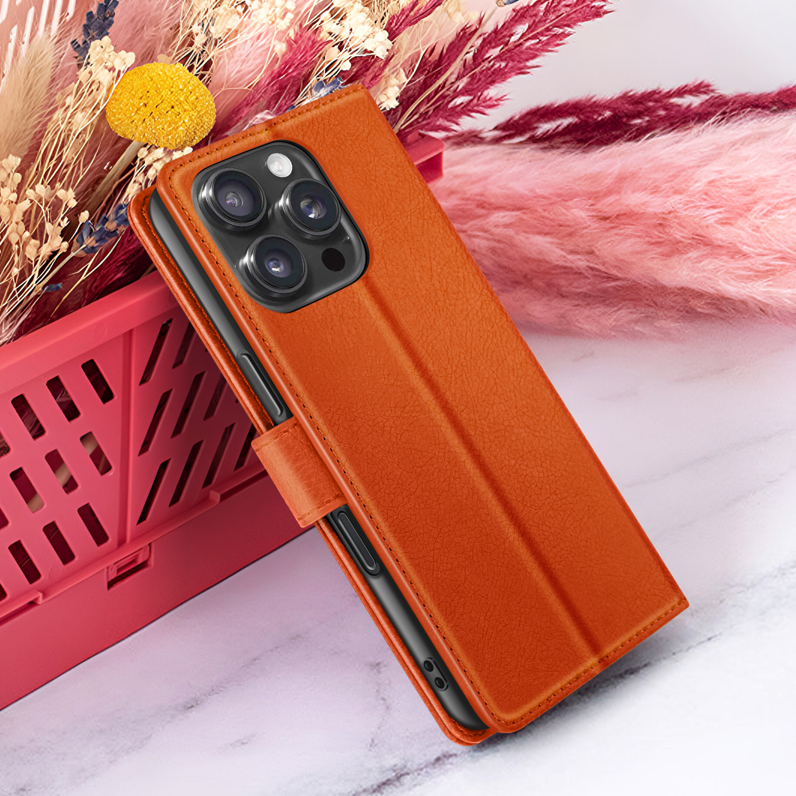Una custodia arancione con un telefono nero all'interno, su uno sfondo di fiori rosa e bianchi.
