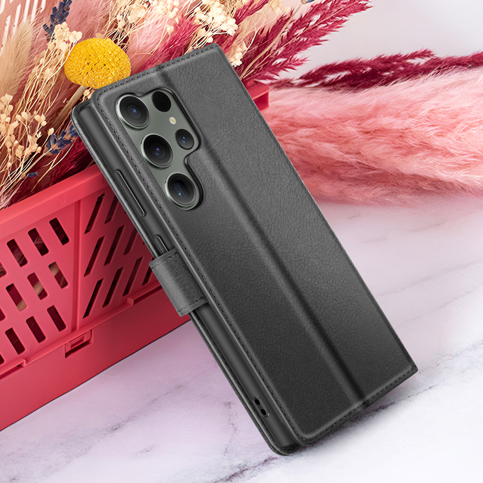 Een zwarte telefoonhoes met een camera-uitsparing. Het wordt gepresenteerd voor een roze en rode bloemenarrangement.