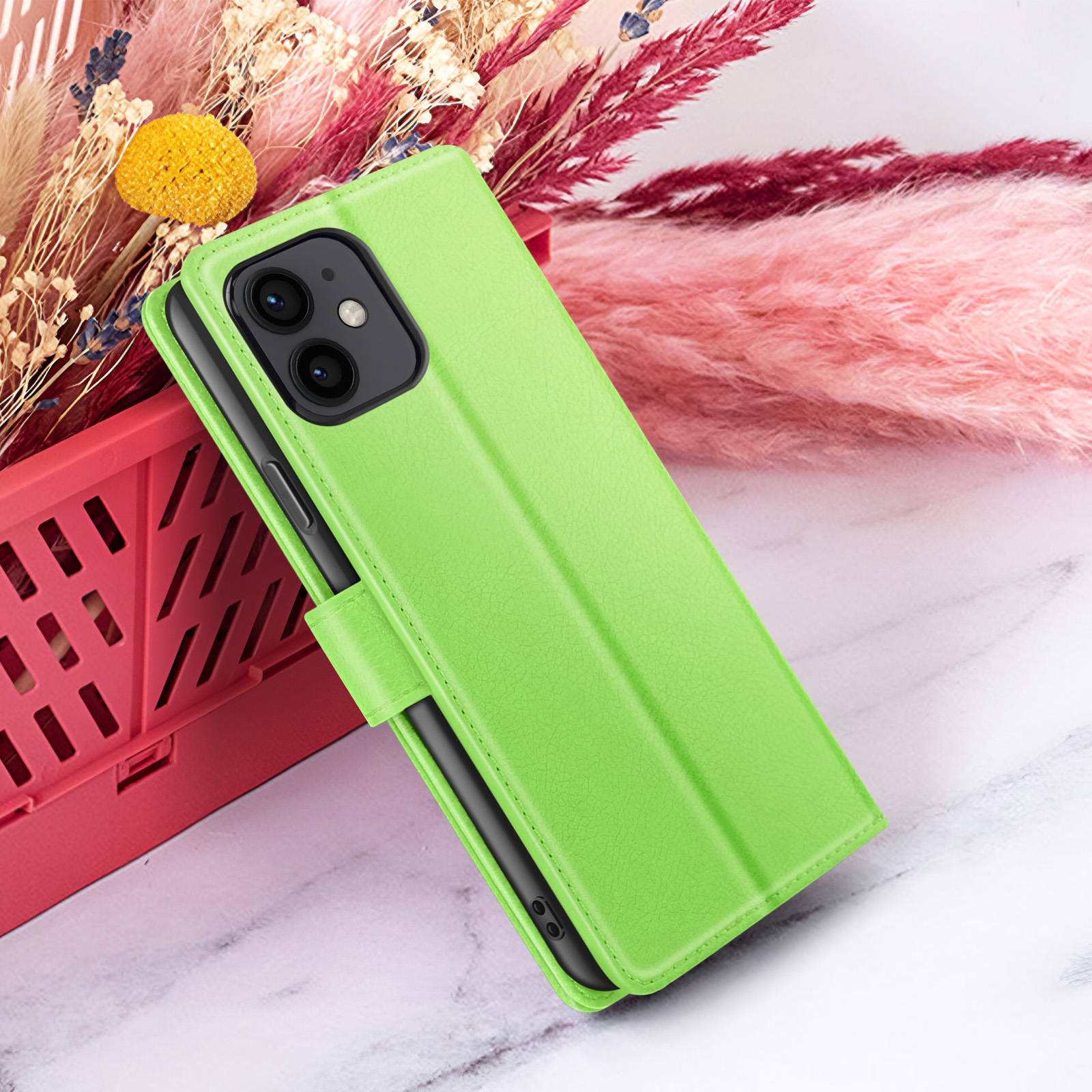 Un étui de téléphone vert est sur une surface en marbre avec des fleurs roses et blanches en arrière-plan.