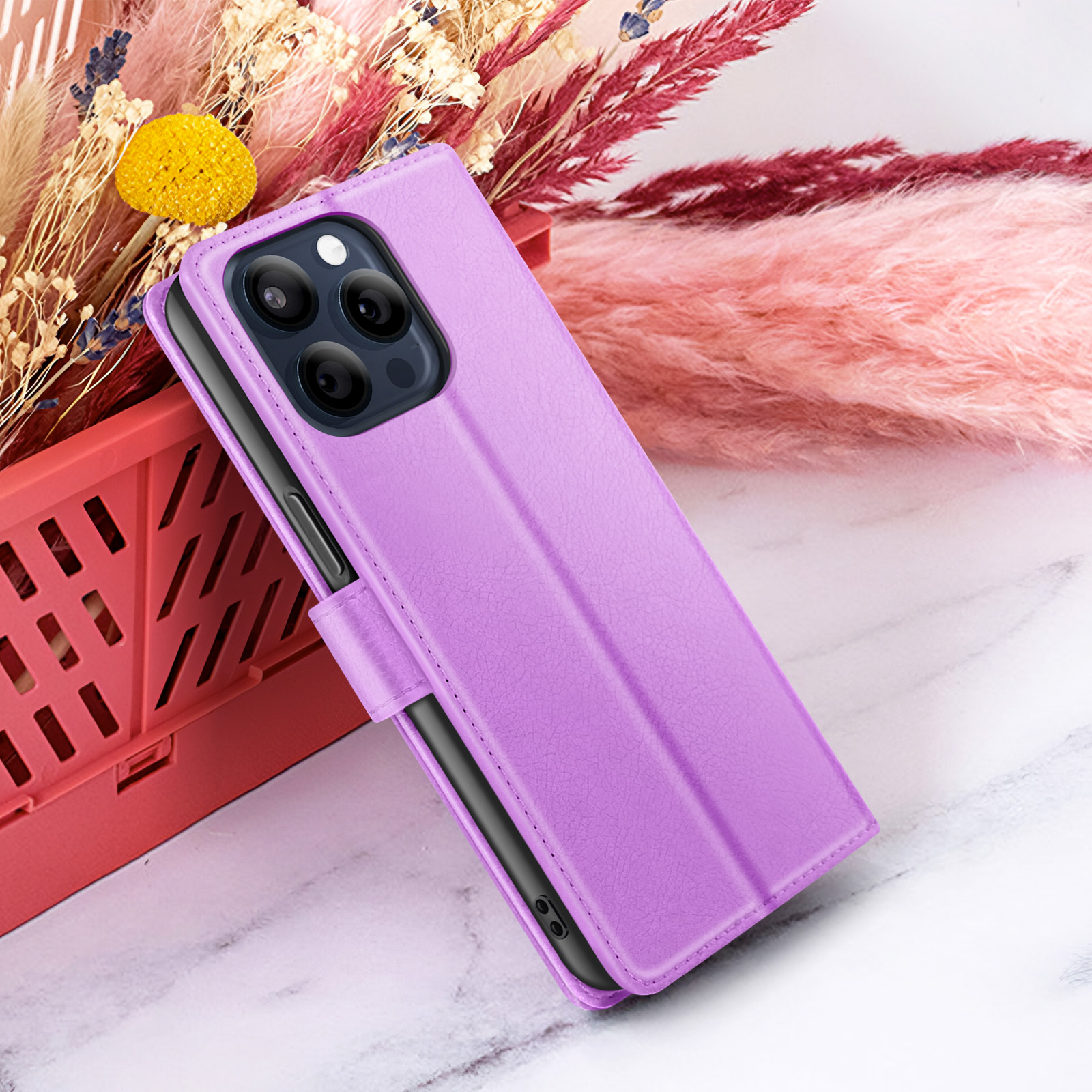 Een paarse telefoonhoes met een telefoon erin, tegen een achtergrond van bloemen en een rode container.