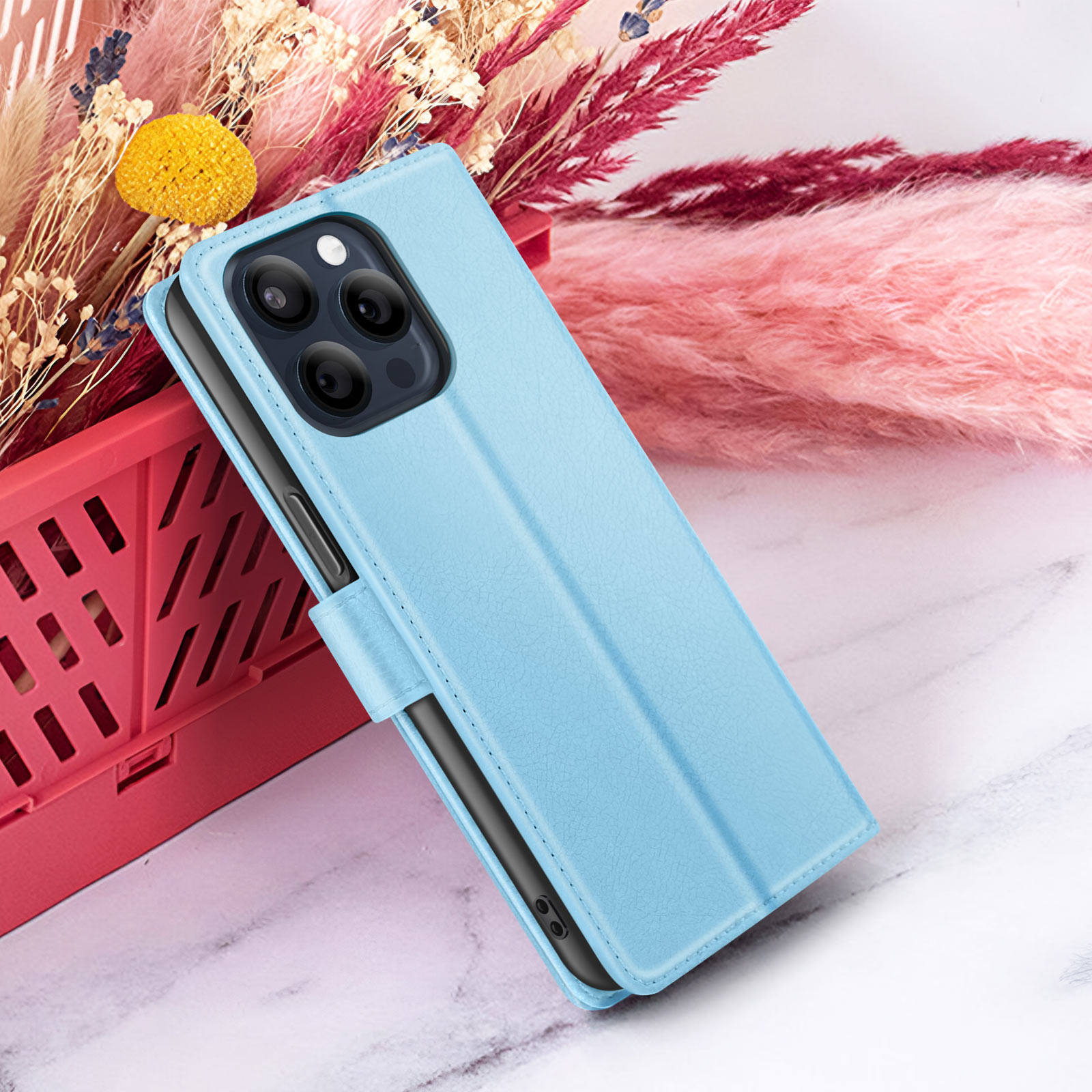 Una custodia per telefono azzurra è aperta, rivelando un telefono. Lo sfondo ha fiori rosa, un cestino rosso e superficie in marmo.