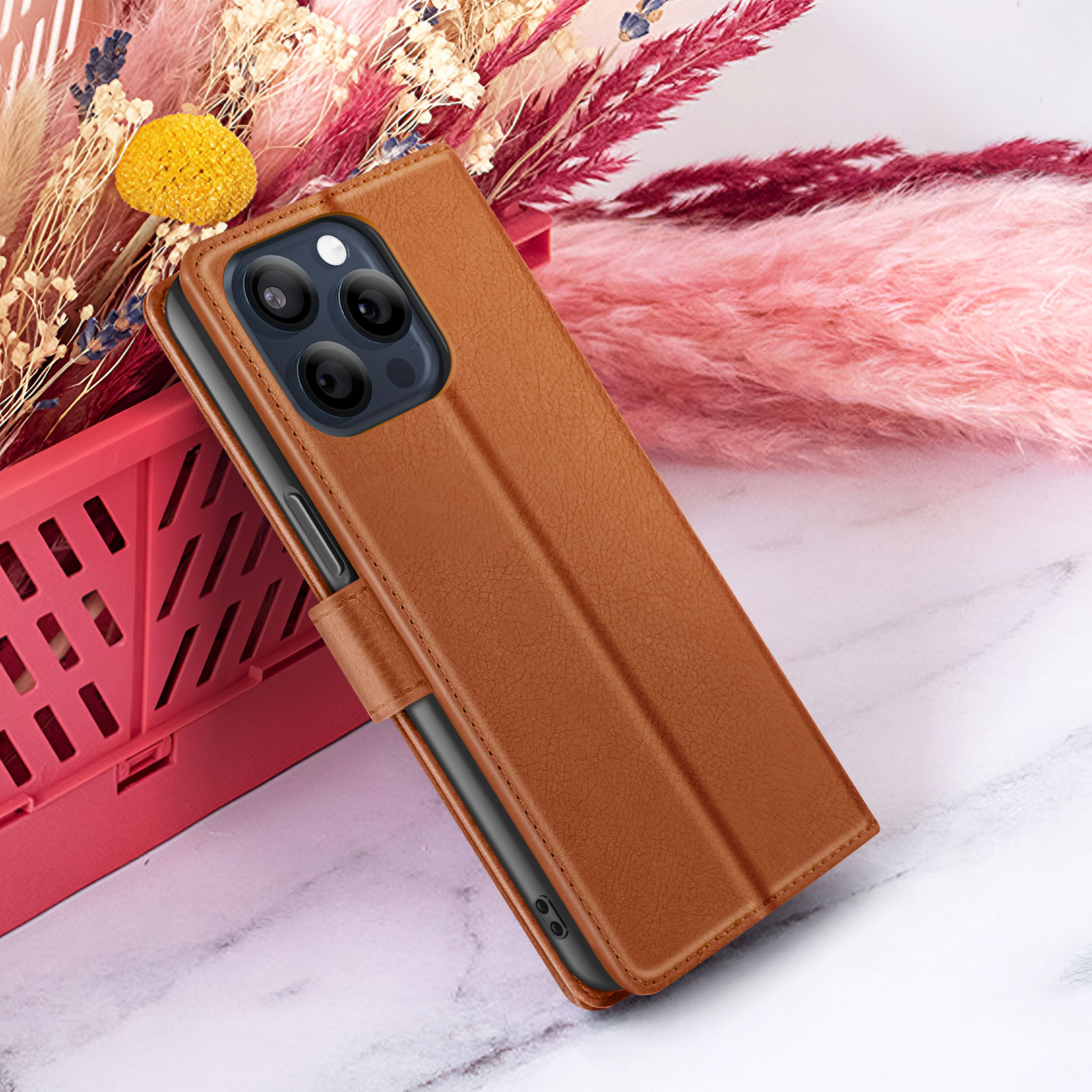 Bruine telefoonhoes met telefoon, op marmer met roze bloemen en rode mand op de achtergrond.