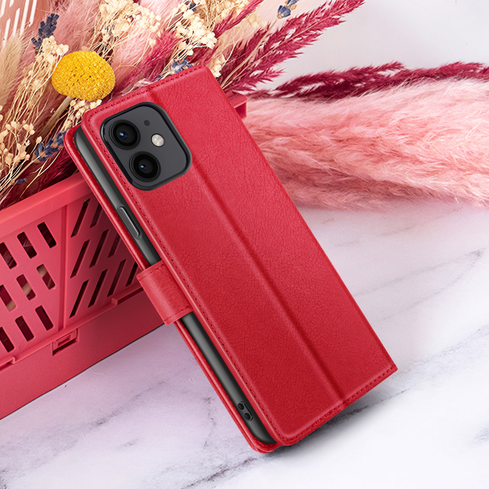 Een rode telefoonhoes met een zwarte telefoon erin ligt naast decoratieve bloemen. De achtergrond is lichtroze en wit.