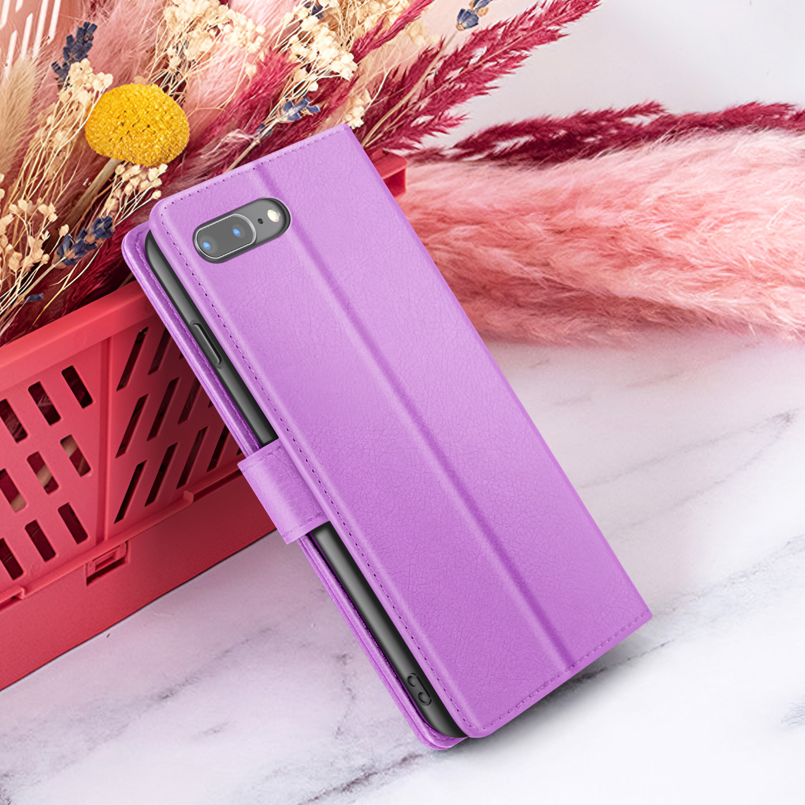 Un étui de téléphone violet sur une surface en marbre avec des fleurs séchées et un panier rouge en arrière-plan.