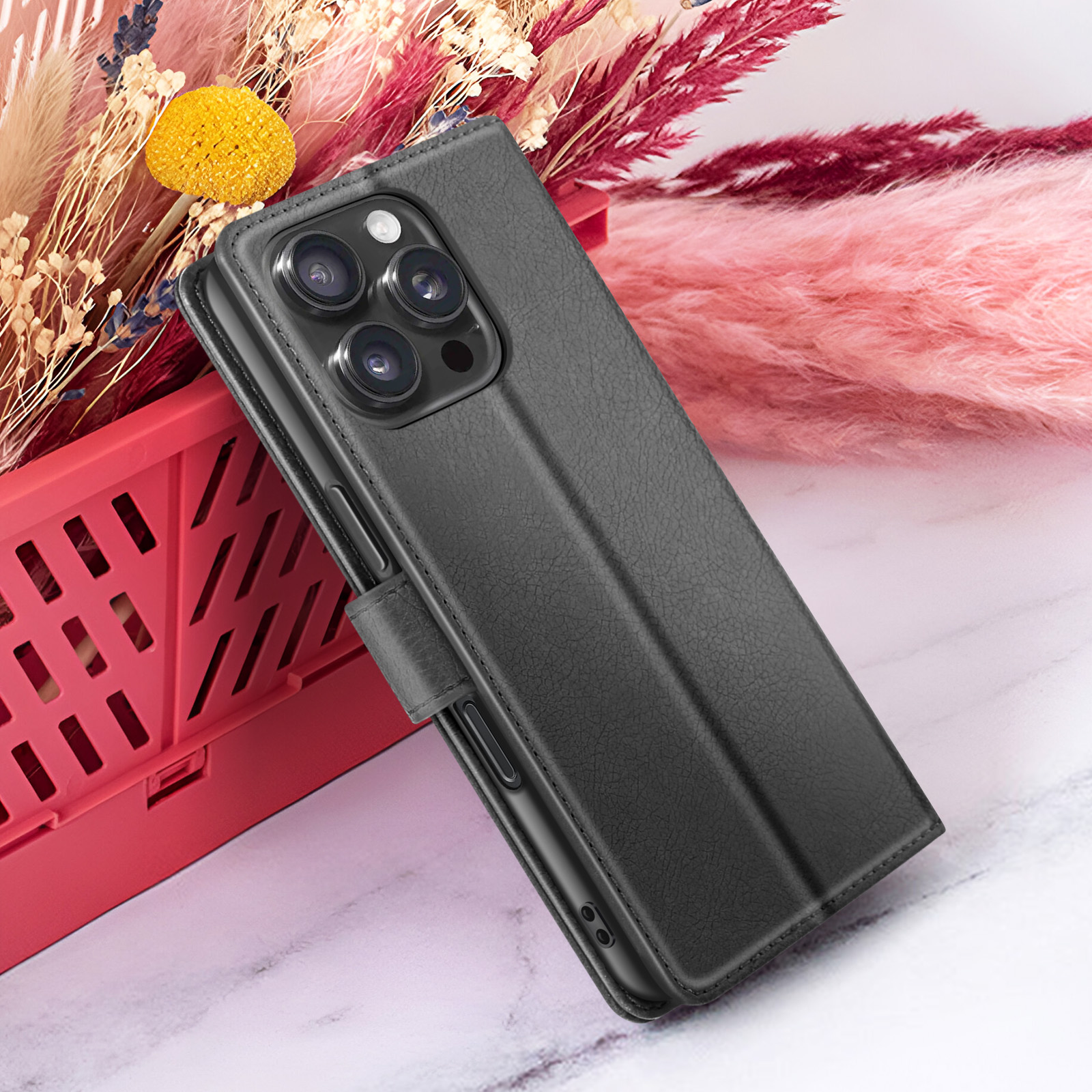 Zwarte telefoonhoes met cameralenzen op marmer, rode mand en gedroogde bloemen.
