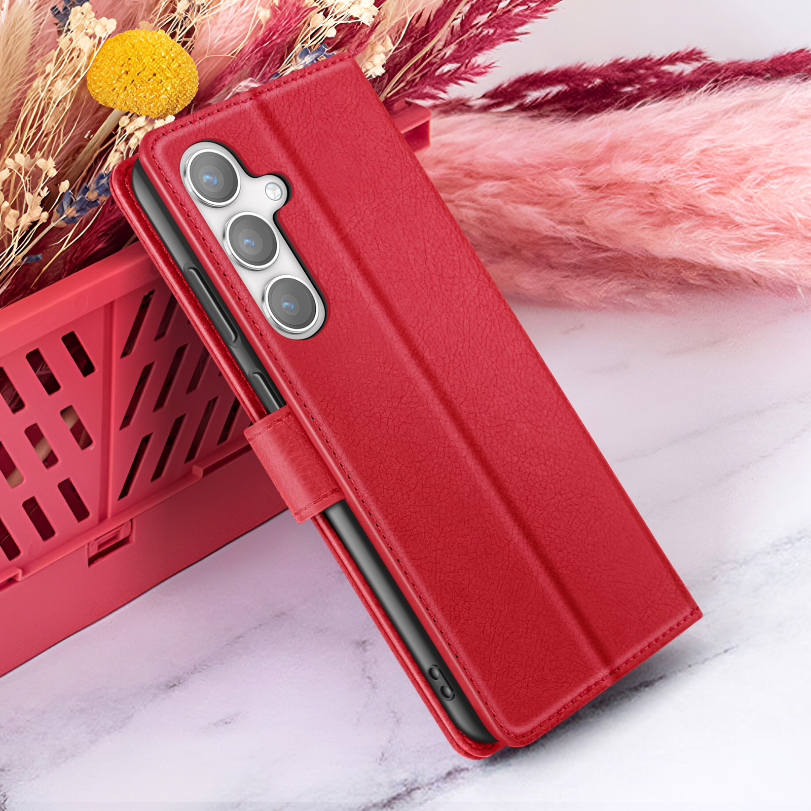 Étui de téléphone rouge avec un téléphone à l'intérieur. Une caisse rouge et des fleurs en arrière-plan. Surface en marbre.