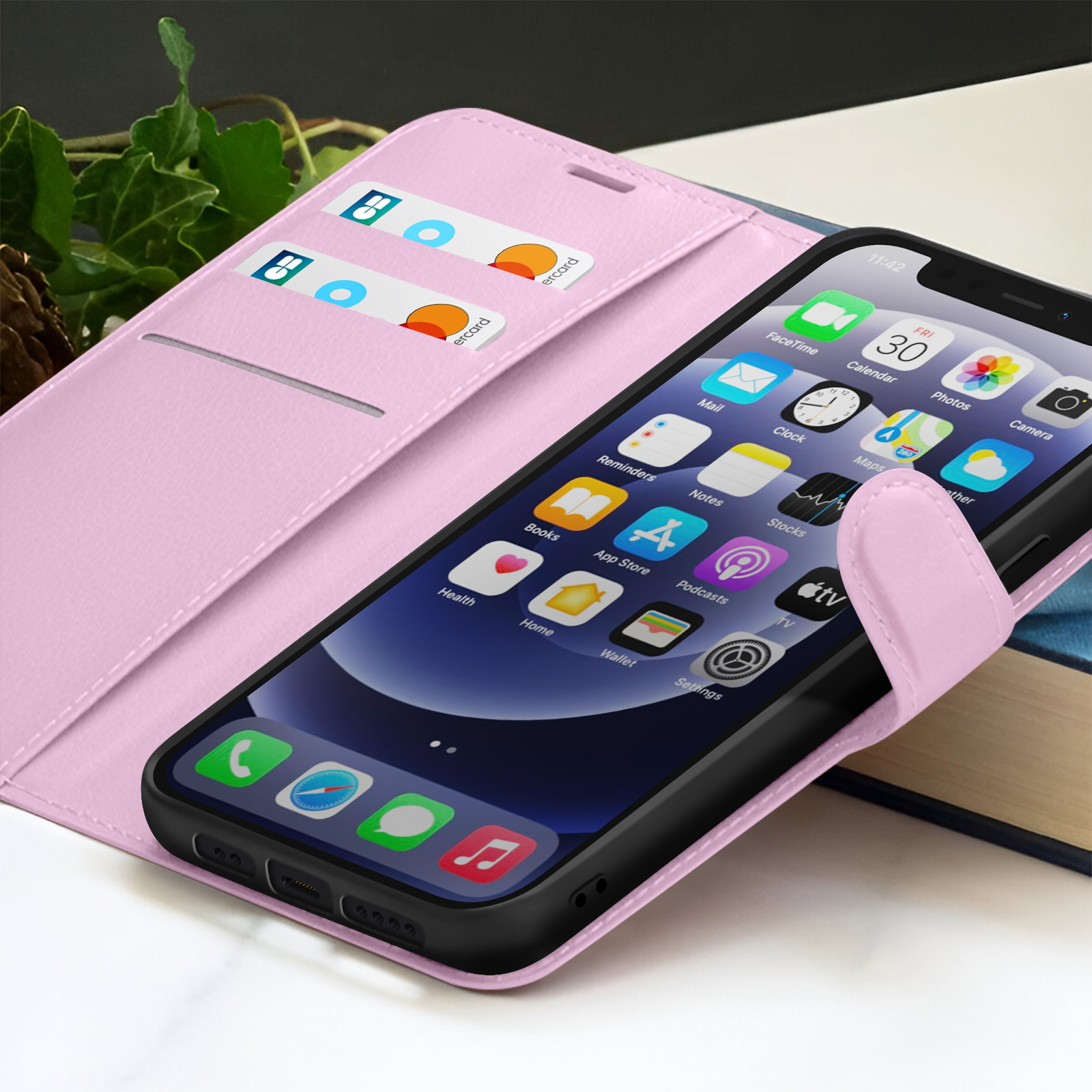 iPhone in roze hoes, met app-iconen. Creditcards zichtbaar in de hoes. Achtergrond: bladeren en een boek.