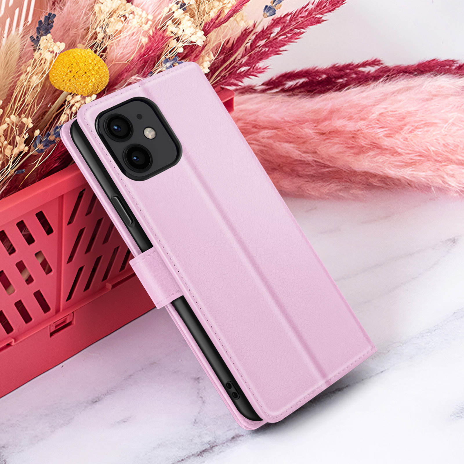 Roze telefoonhoesje op een marmeren oppervlak, met gedroogde bloemen op de achtergrond en een rode mand.