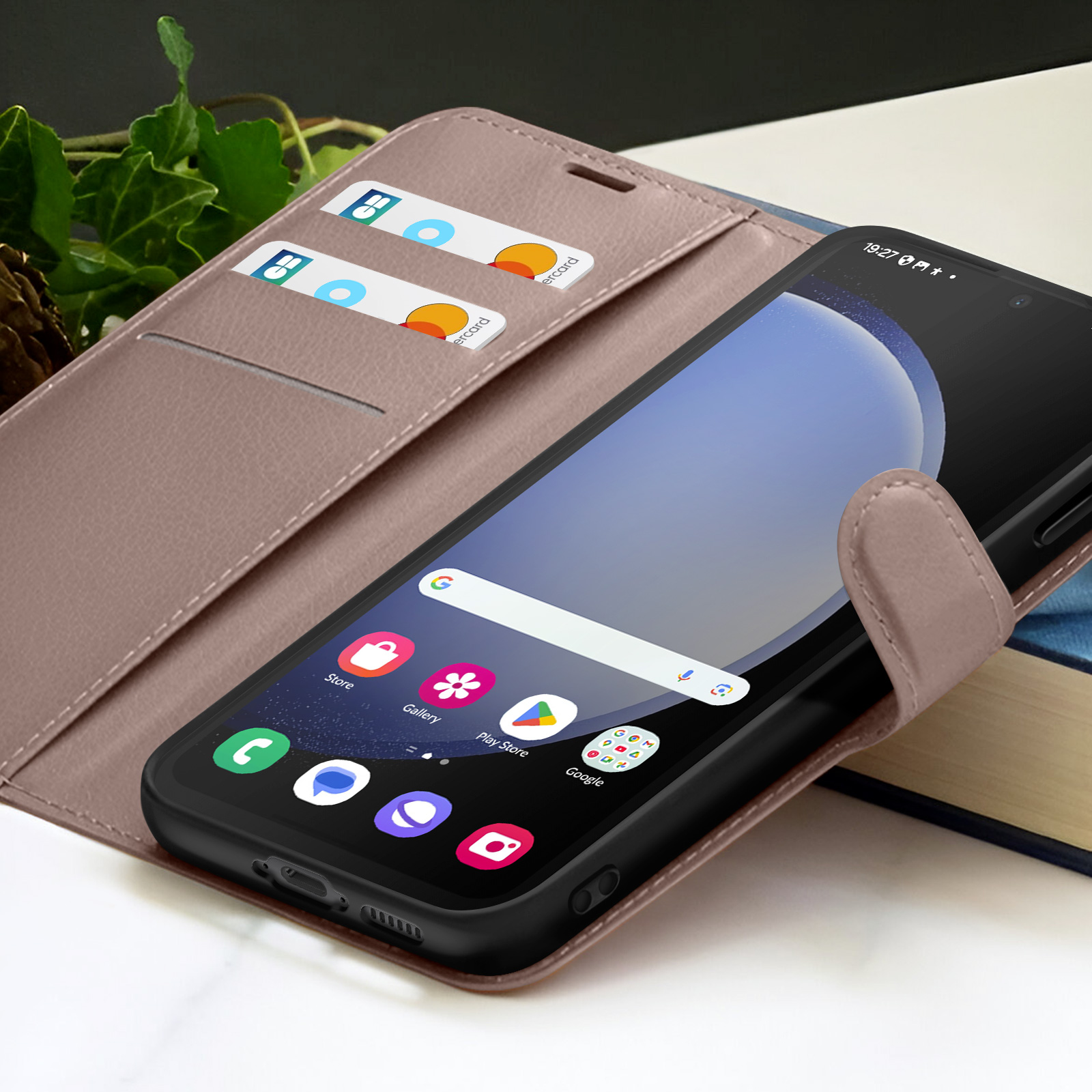 Smartphone dans un étui marron avec cartes de crédit. L'écran affiche des icônes d'applications. Fond : lierre, table et livre.