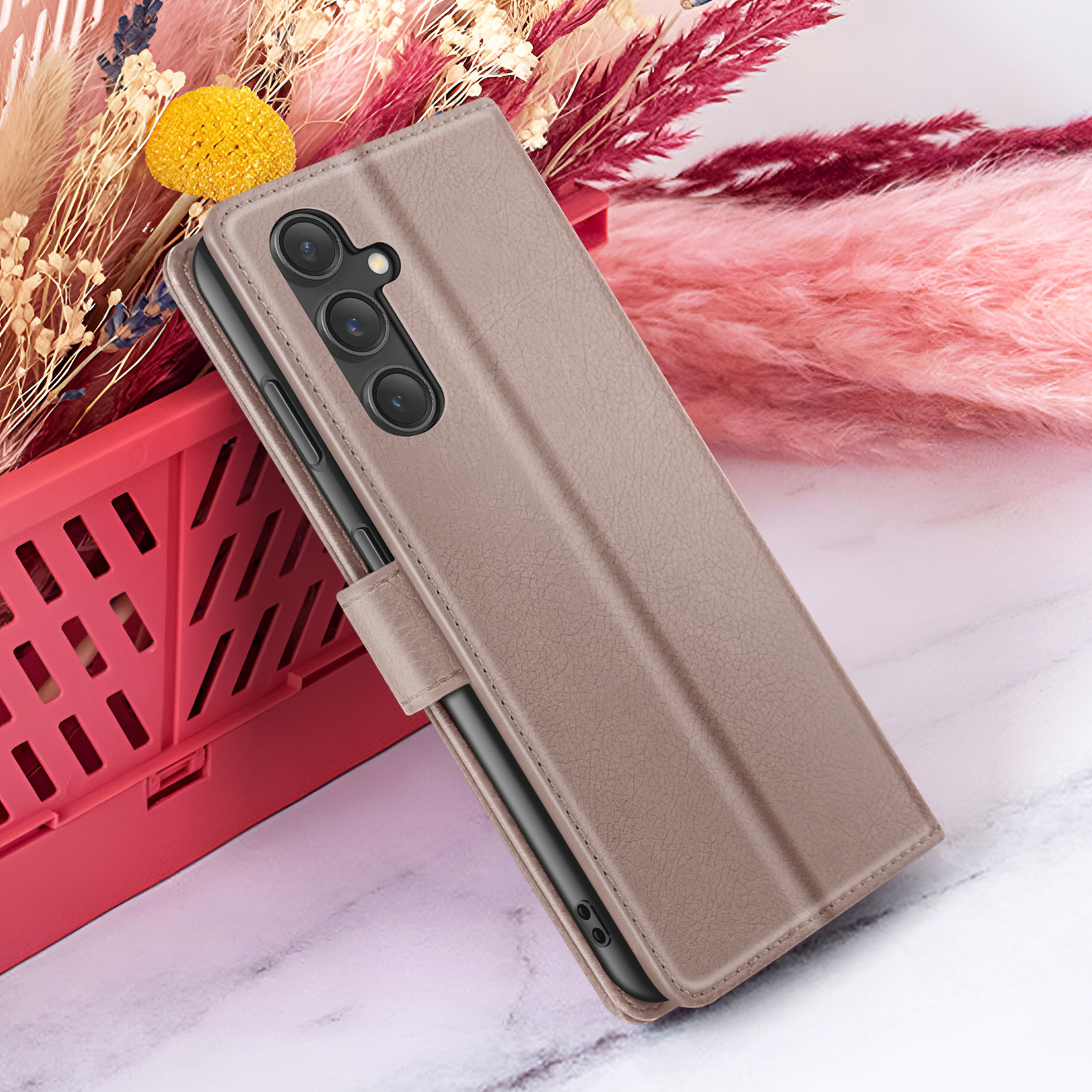 Un étui de téléphone est appuyé contre un panier avec un fond floral. L'étui est marron et le fond a des couleurs roses et rouges.