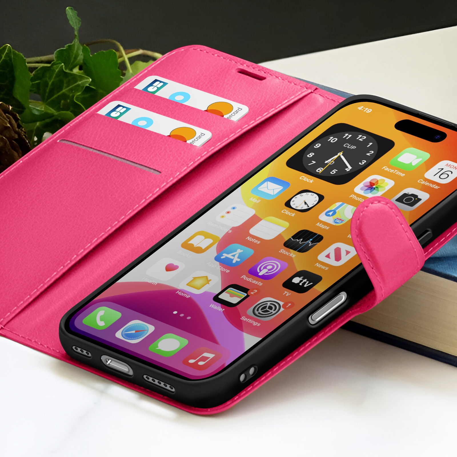 Una custodia rosa per telefono con un telefono che mostra le icone delle app è aperta. Ci sono carte nella custodia. Un libro sullo sfondo.