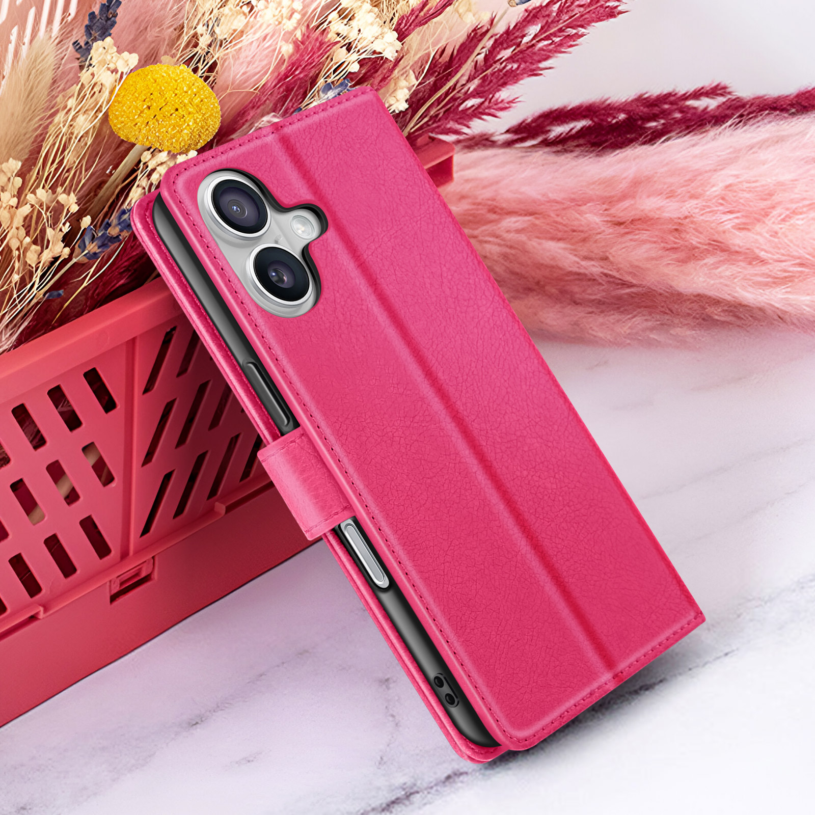 Una custodia rosa per telefono, aperta, poggia su una cassa rosa. Fiori secchi sullo sfondo.