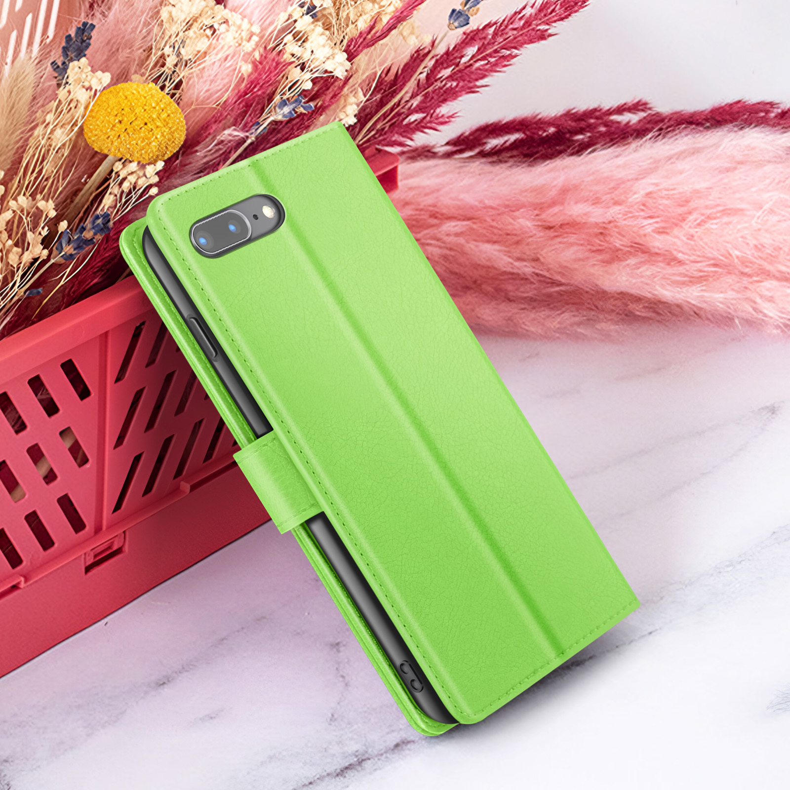 Een groene telefoonhoes met een telefoon erin, tegen een achtergrond van bloemen en een rode mand op marmer.