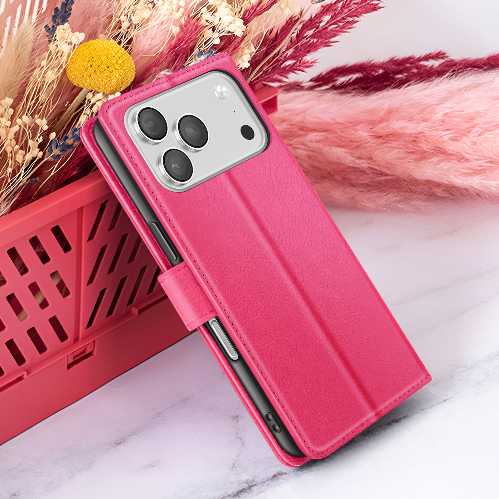 Een roze telefoonhoesje met een telefoon erin ligt op een marmeren oppervlak. Achtergrond bevat roze en beige gedroogde bloemen.