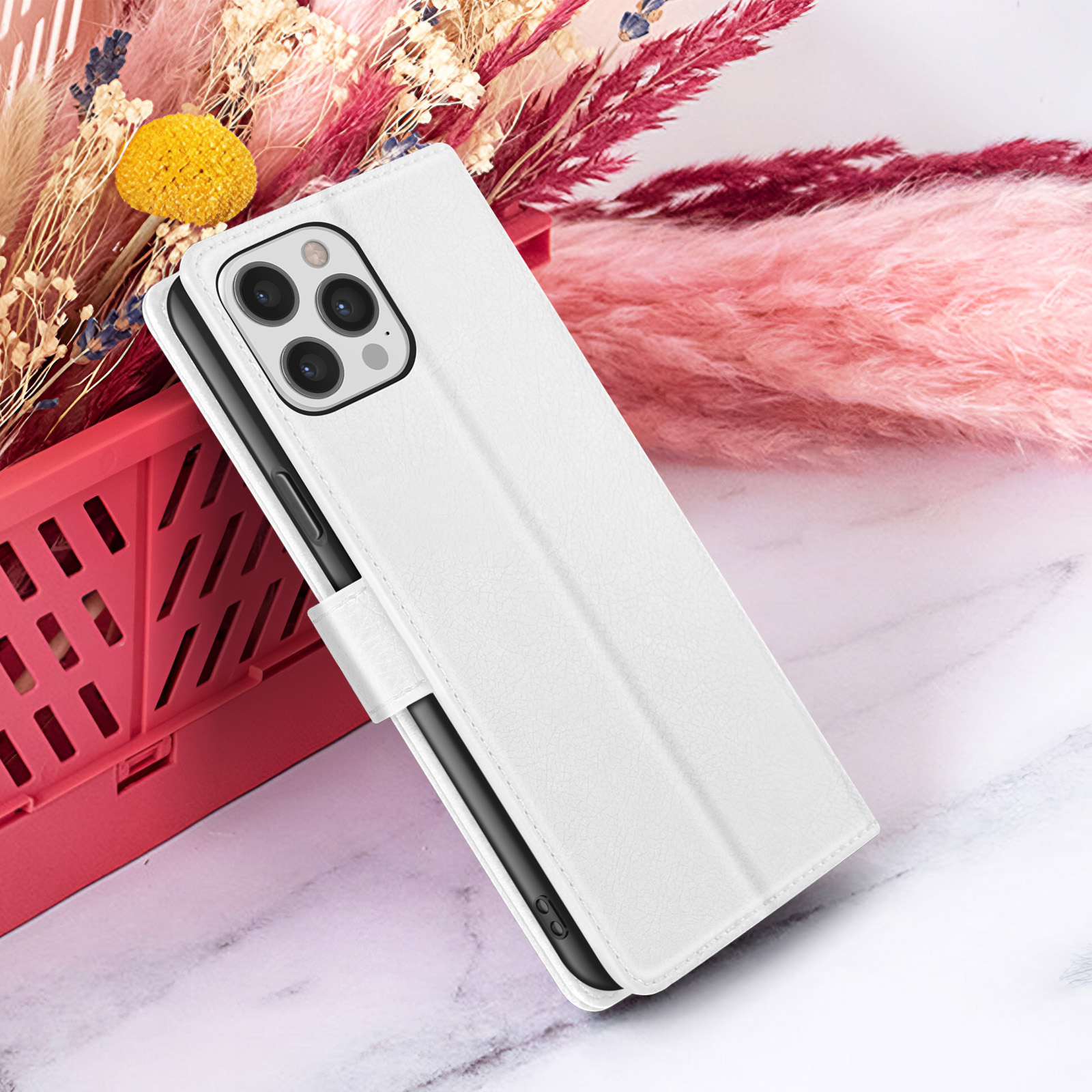 Una custodia bianca per telefono con patta chiusa poggia su una superficie di marmo, con uno sfondo di fiori secchi rosa e beige.