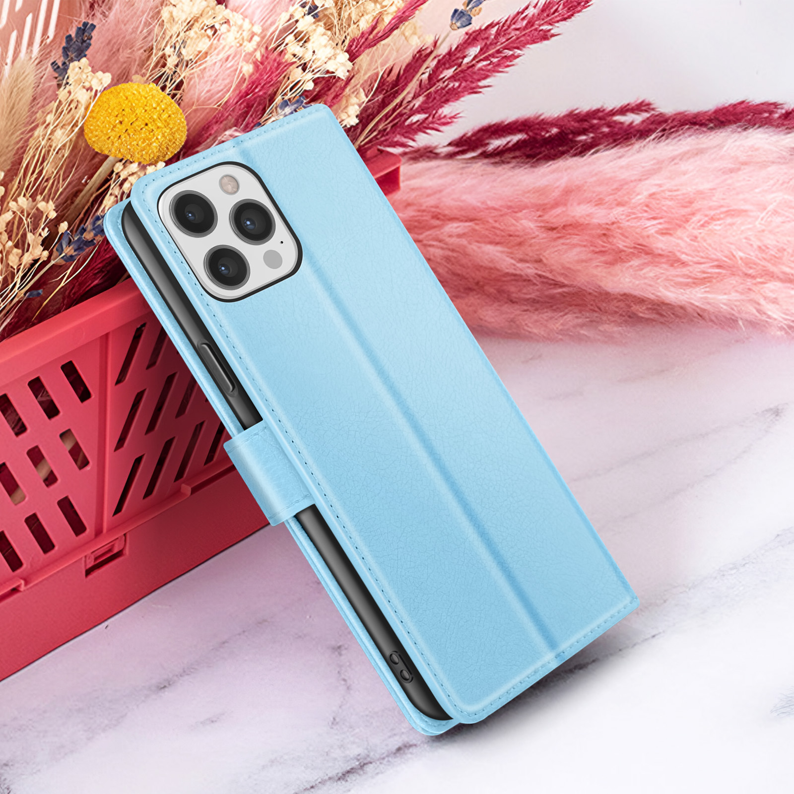Un étui de téléphone bleu clair avec un téléphone noir à l'intérieur. L'étui est appuyé contre une composition florale.