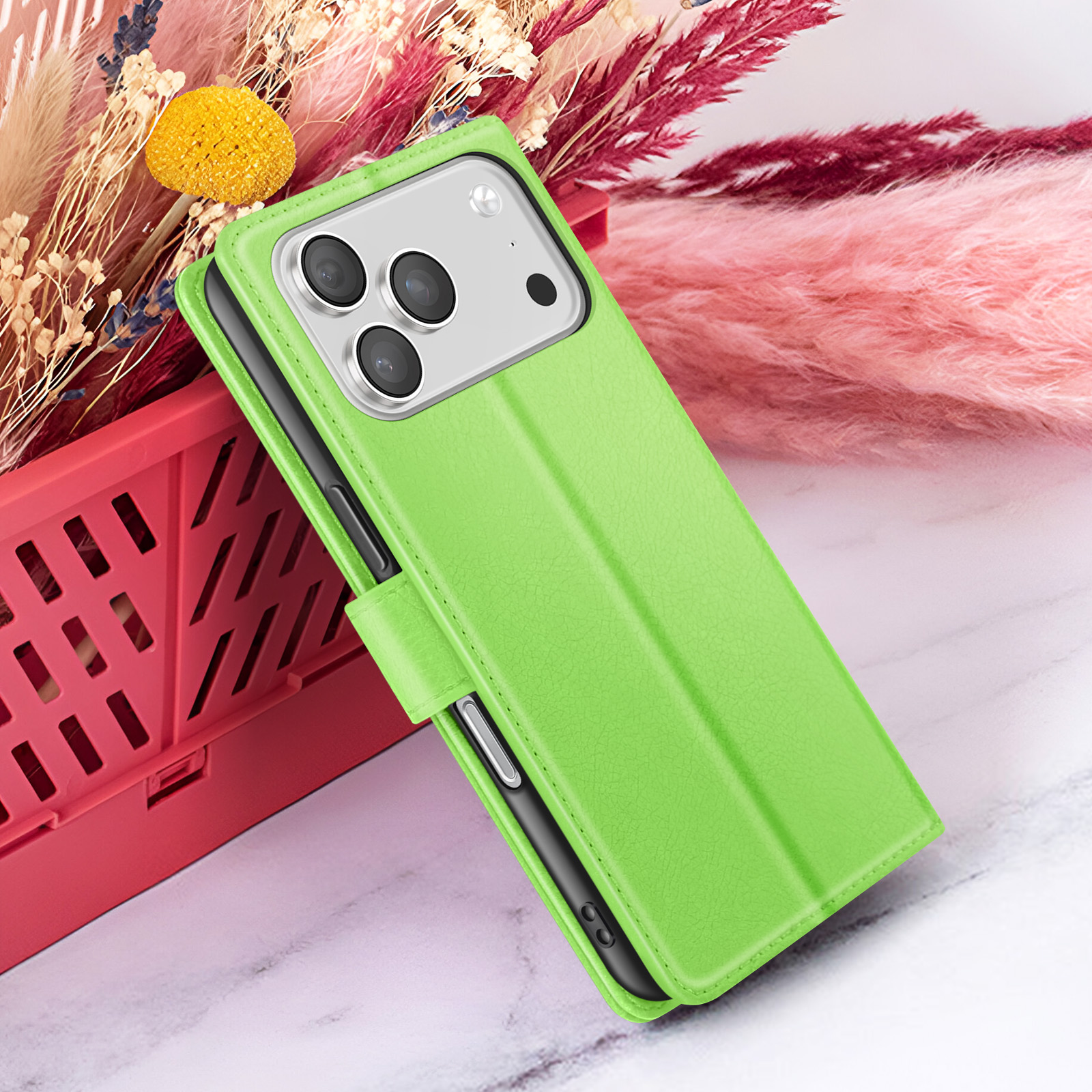 Een groene telefoonhoes leunt tegen een rode krat. Bloemen in roze en beige tinten op de achtergrond.