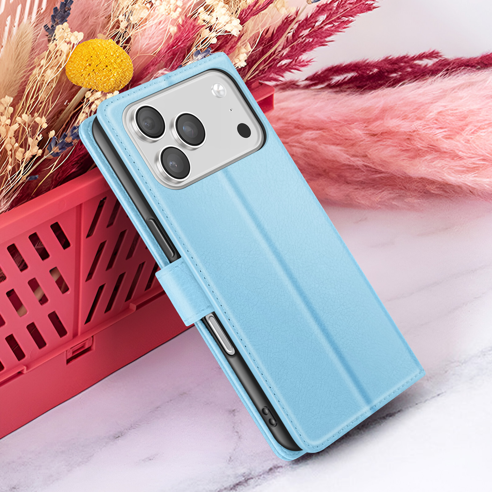 Een lichtblauwe telefoonhoes met een telefoon erin ligt op een marmeren oppervlak. Achtergrond laat bloemen en een rode container zien.