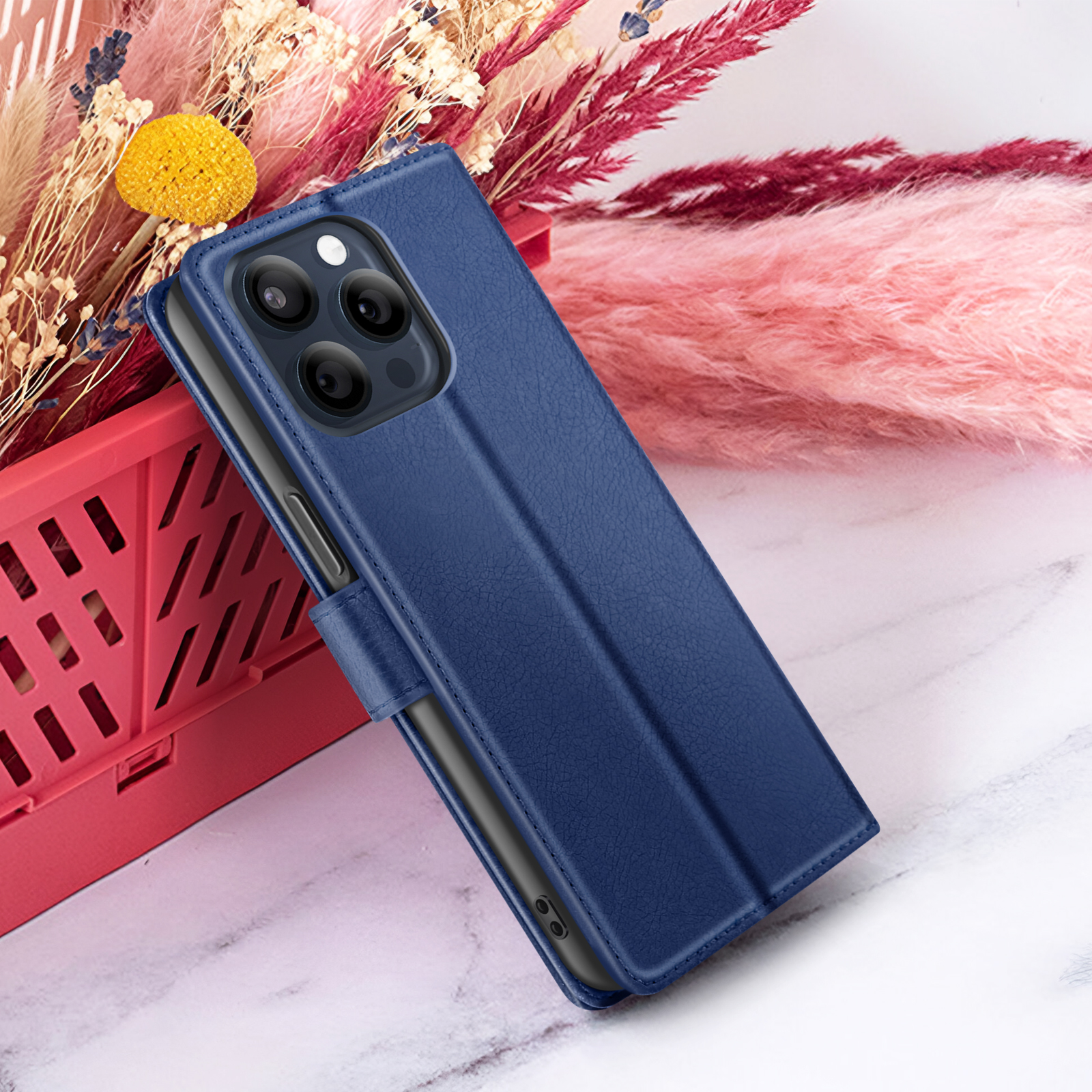 Un étui de téléphone bleu avec un téléphone à l'intérieur, à côté de fleurs roses et beiges, sur une surface en marbre.