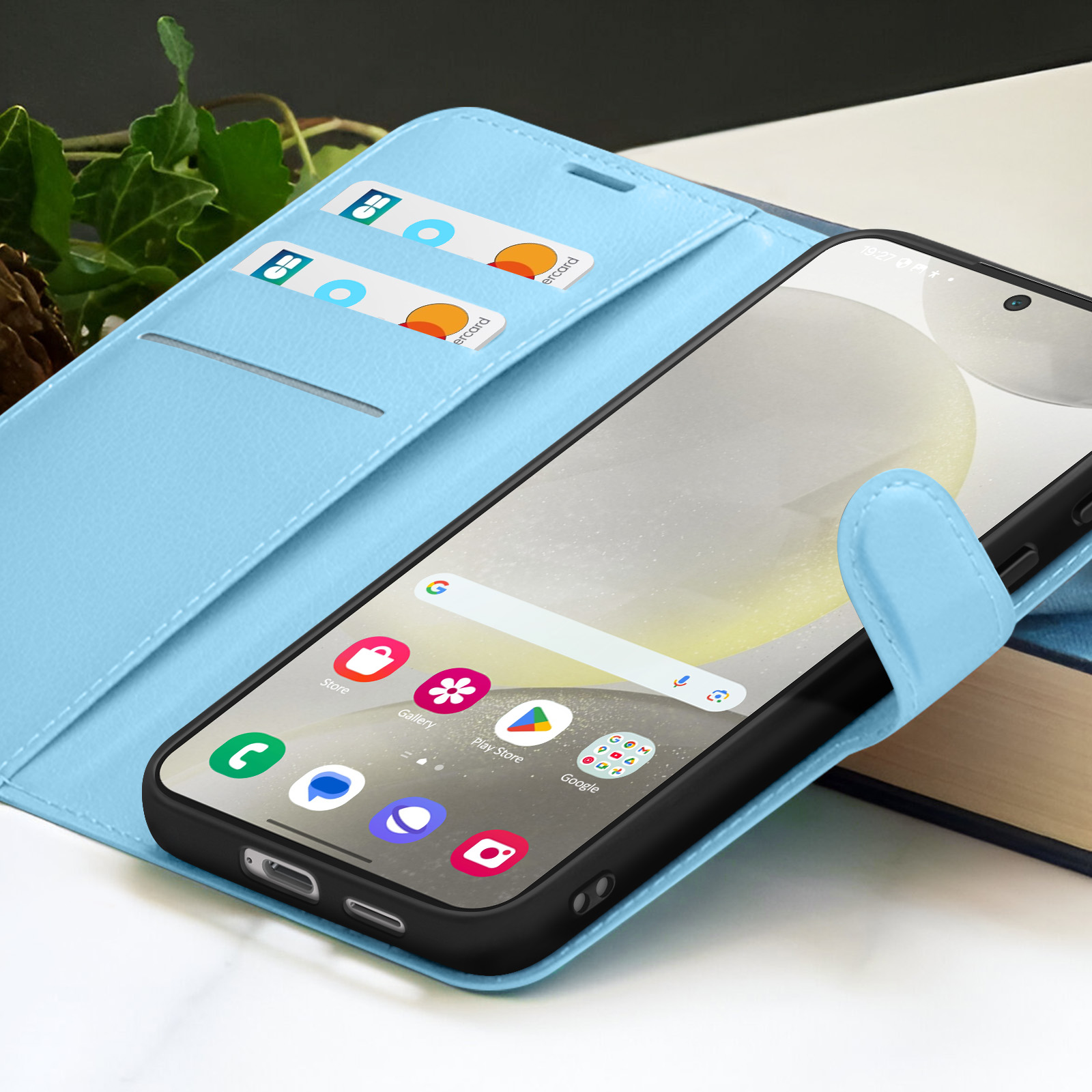Un smartphone avec des applications dans un étui bleu clair. Des cartes de crédit sont dans l'étui. Un livre à droite.