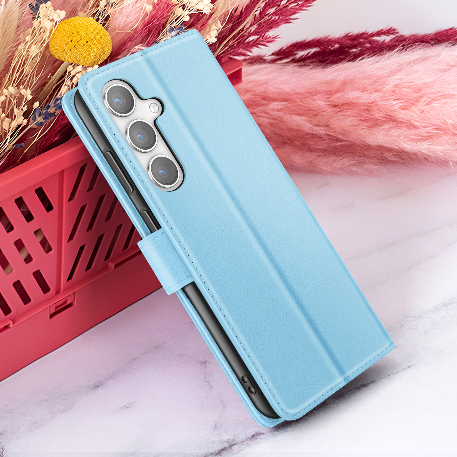 Un étui de téléphone bleu clair avec un appareil photo à trois objectifs, devant des décorations florales roses et rouges.