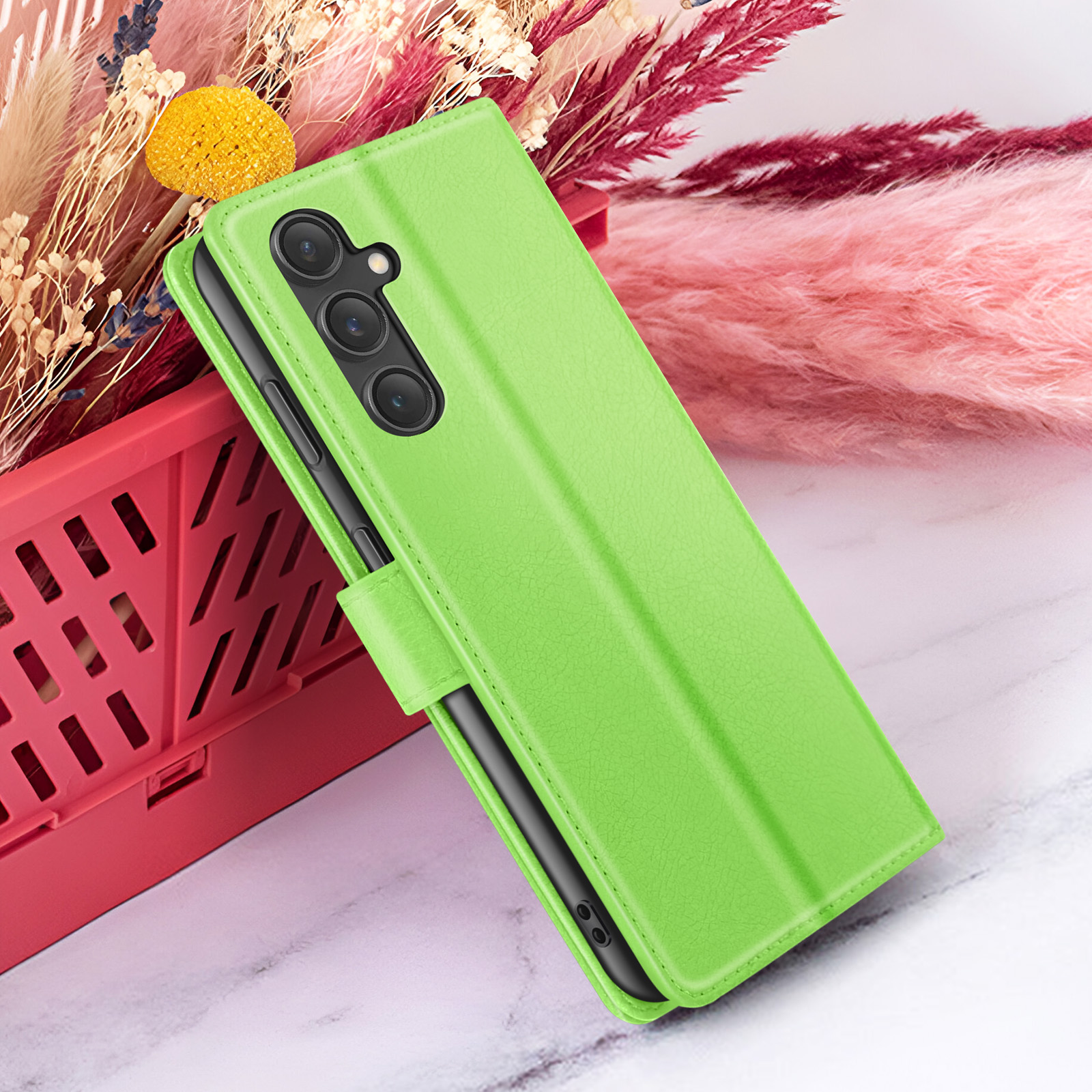 Coque de téléphone verte avec un téléphone à l'intérieur, dans un panier rouge, à côté de fleurs roses et violettes.